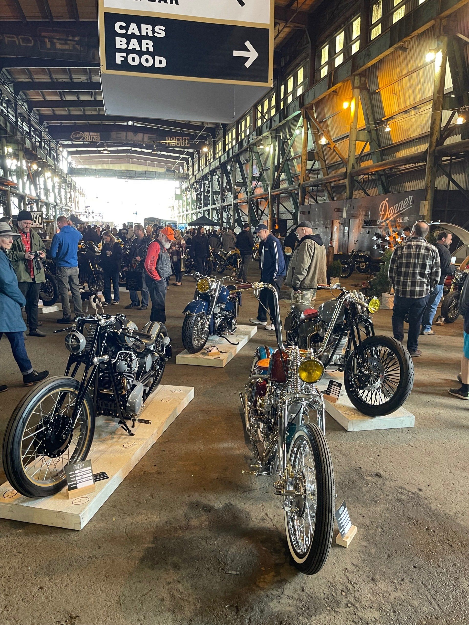 Motorcycles on display in a busy indoor market corridor with a “Café Bar Food” sign overhead