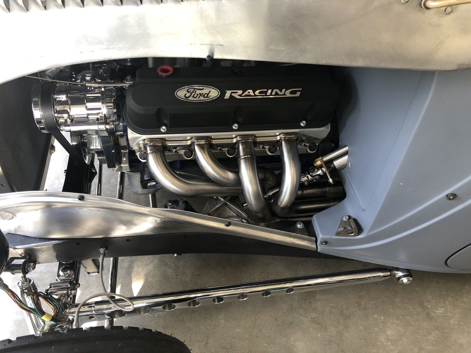 Race car engine bay with exposed chrome exhaust headers and black engine cover.