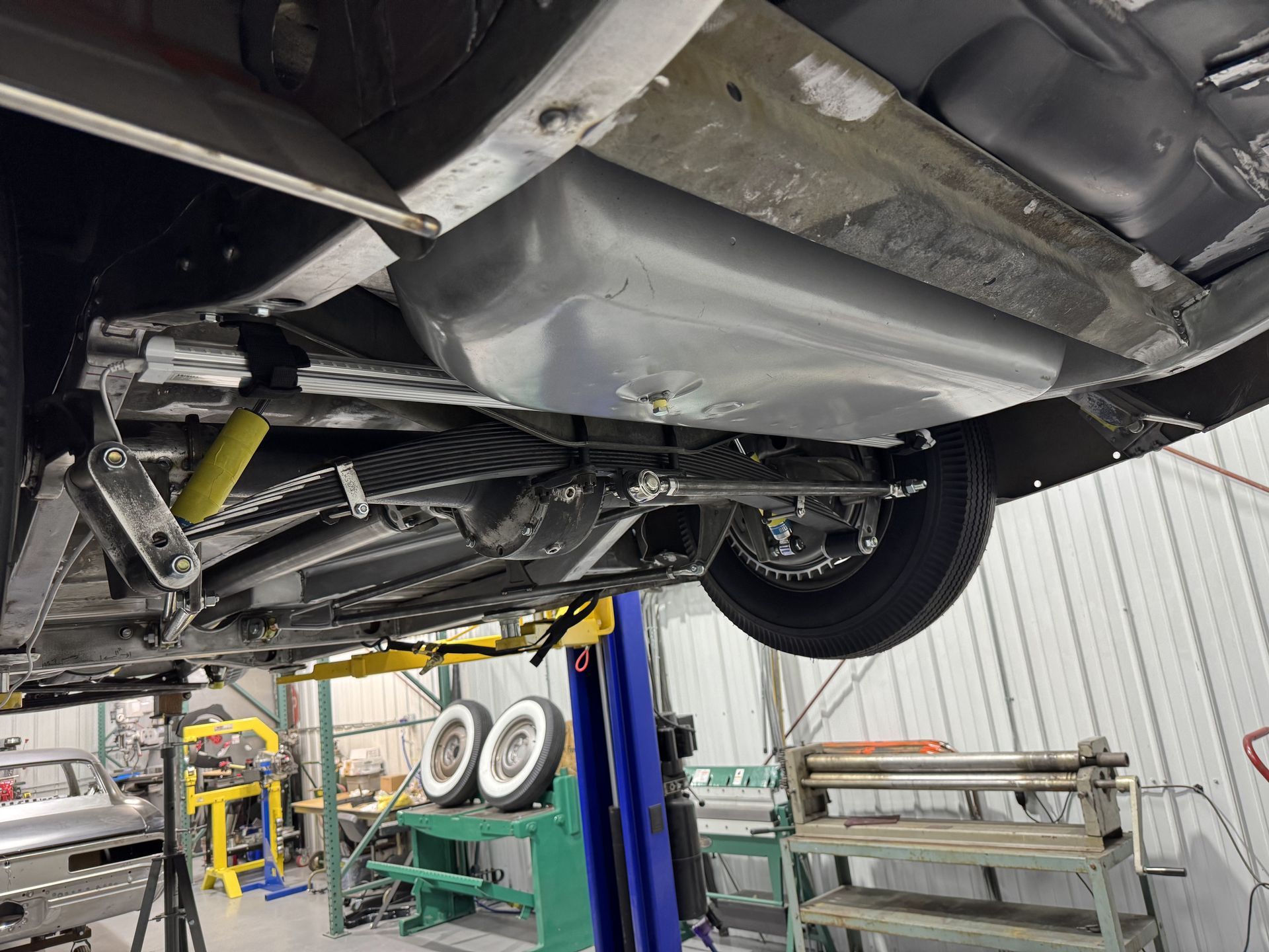 Car underside on a lift in an auto repair shop, showing the exhaust and fuel tank.
