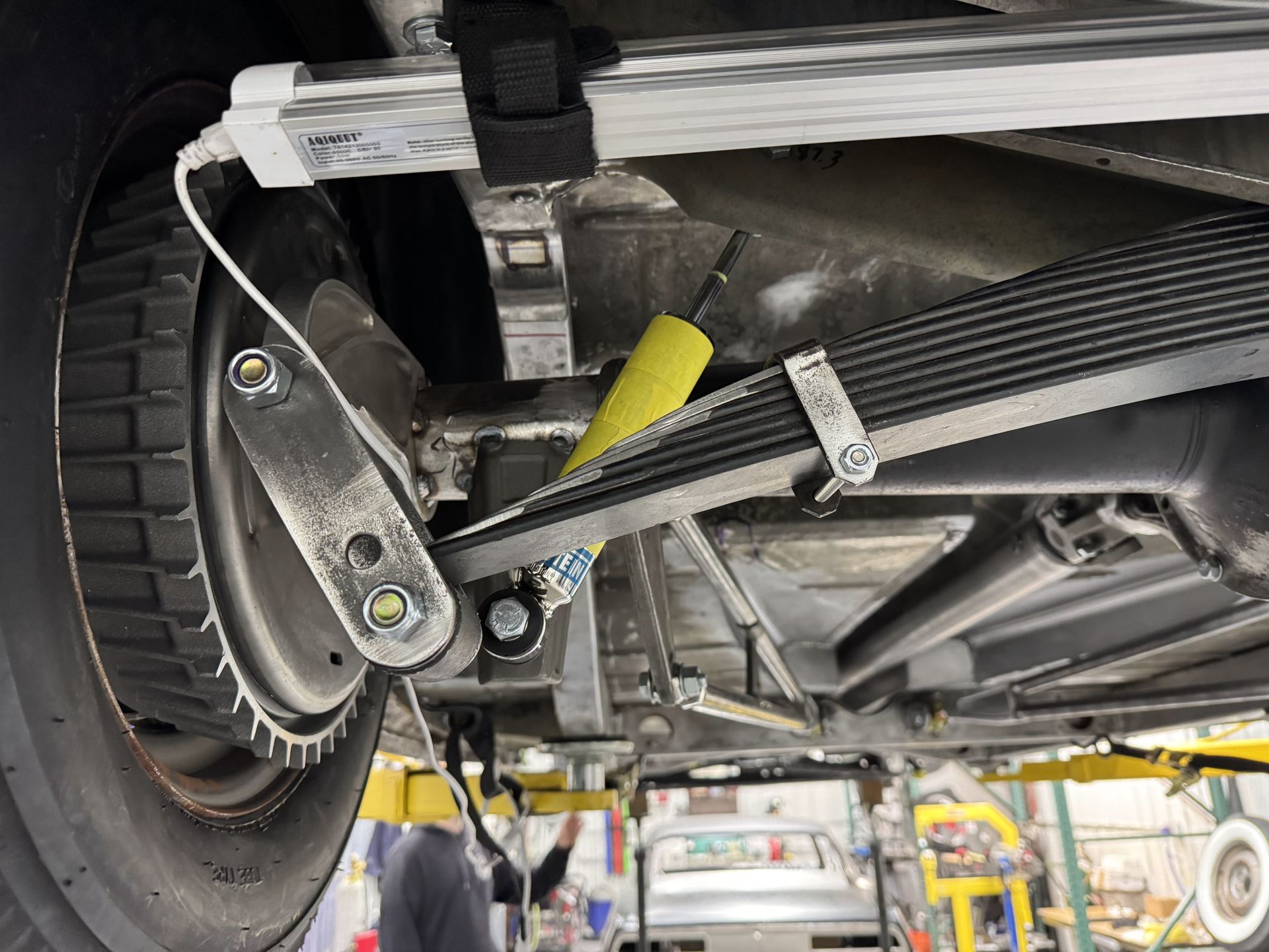 Undercarriage of a vehicle with rear wheel, suspension, and yellow strap in a garage lift area