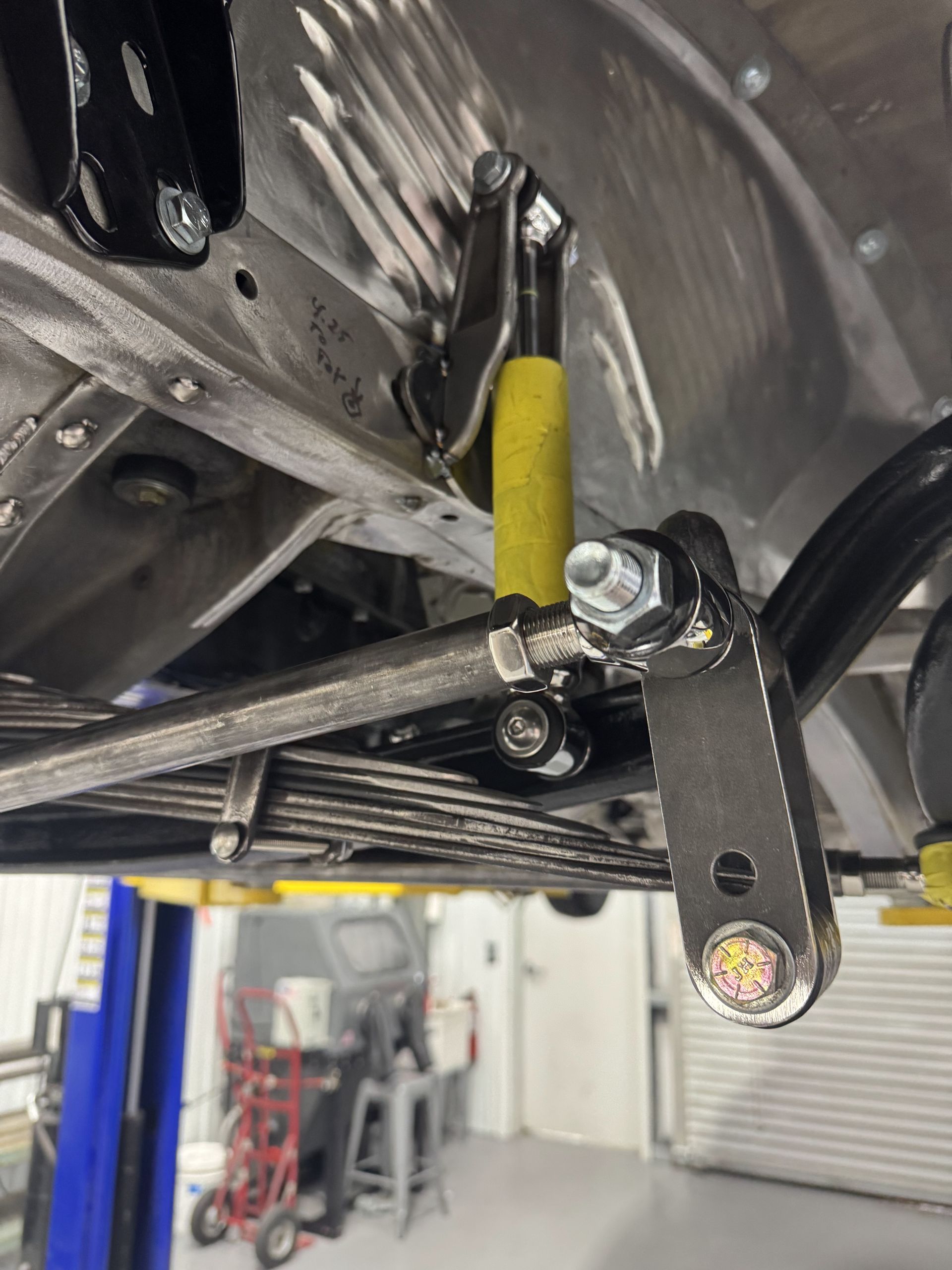 Undercarriage of a vehicle with suspension parts, black control arm, and yellow shock absorber in a workshop