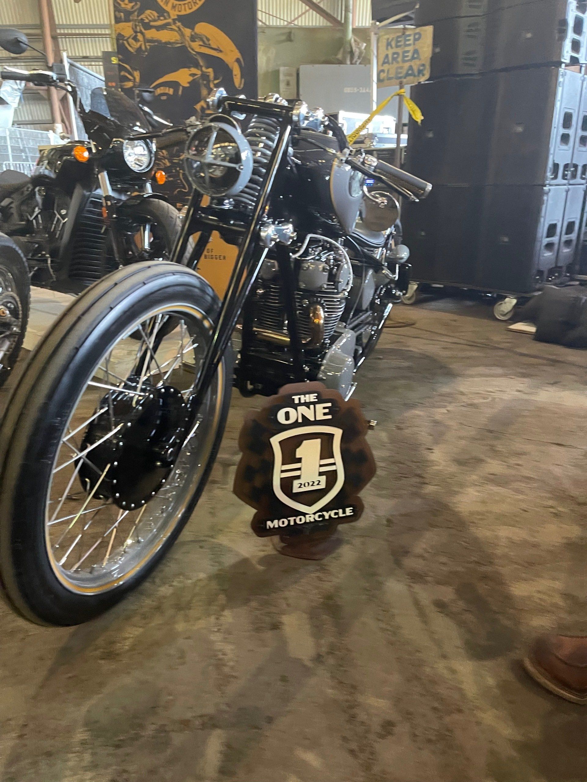 Black custom motorcycle with spoked front wheel parked indoors on a concrete floor.