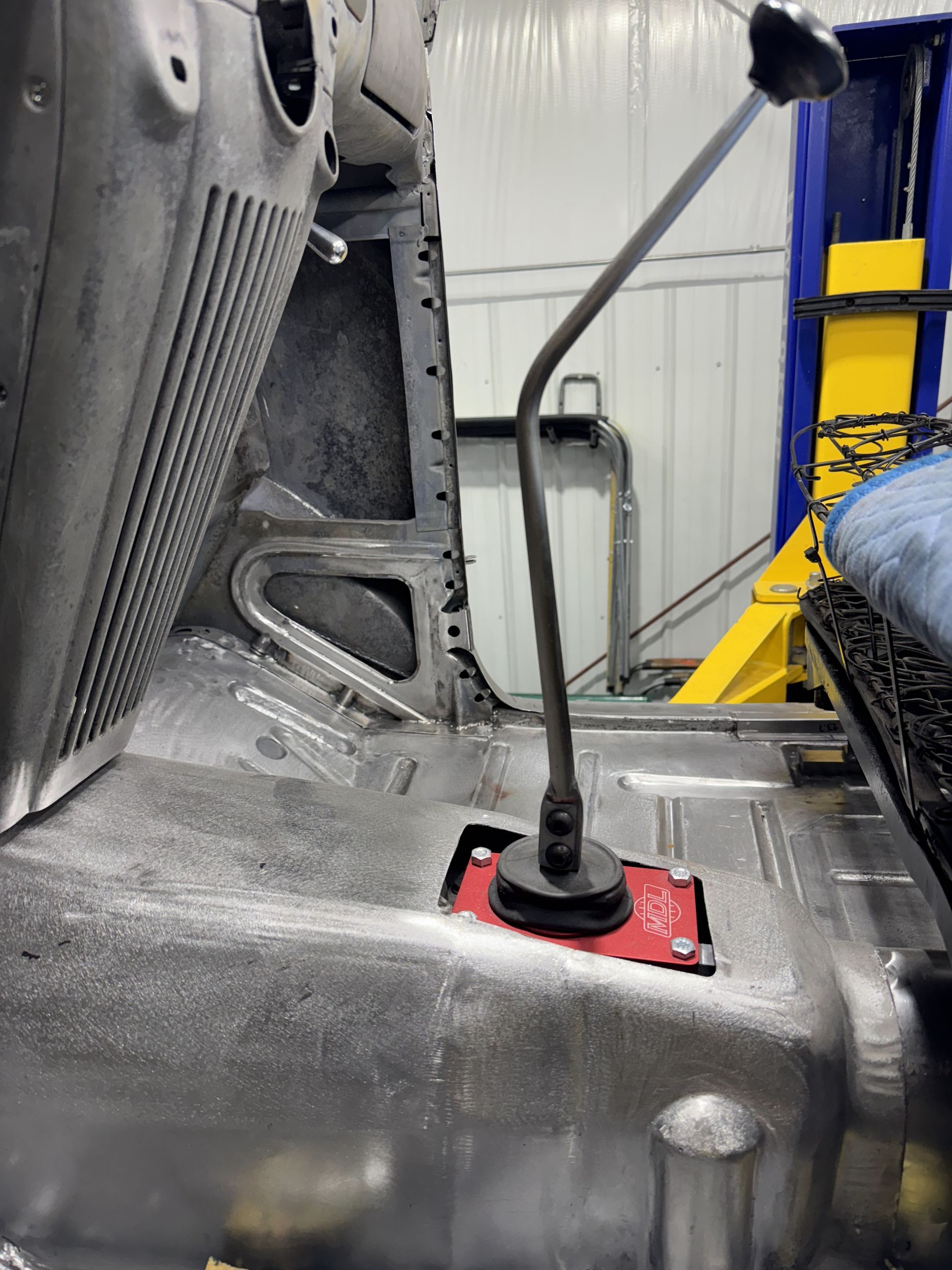 Car interior with a red-and-black floor-mounted gear shifter and gray seats near a blue-and-yellow wall.