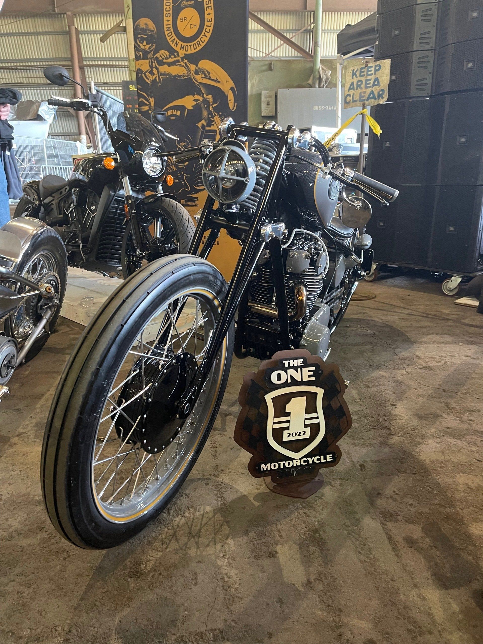 Custom black motorcycles on display at an indoor show, with one front wheel centered in the foreground.