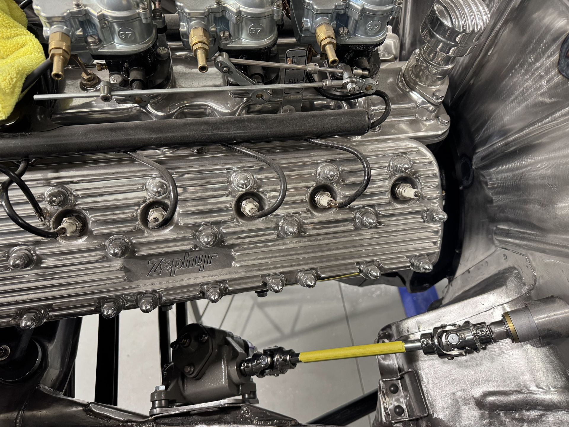Close-up of a silver engine with yellow hoses and black cables in a workshop.