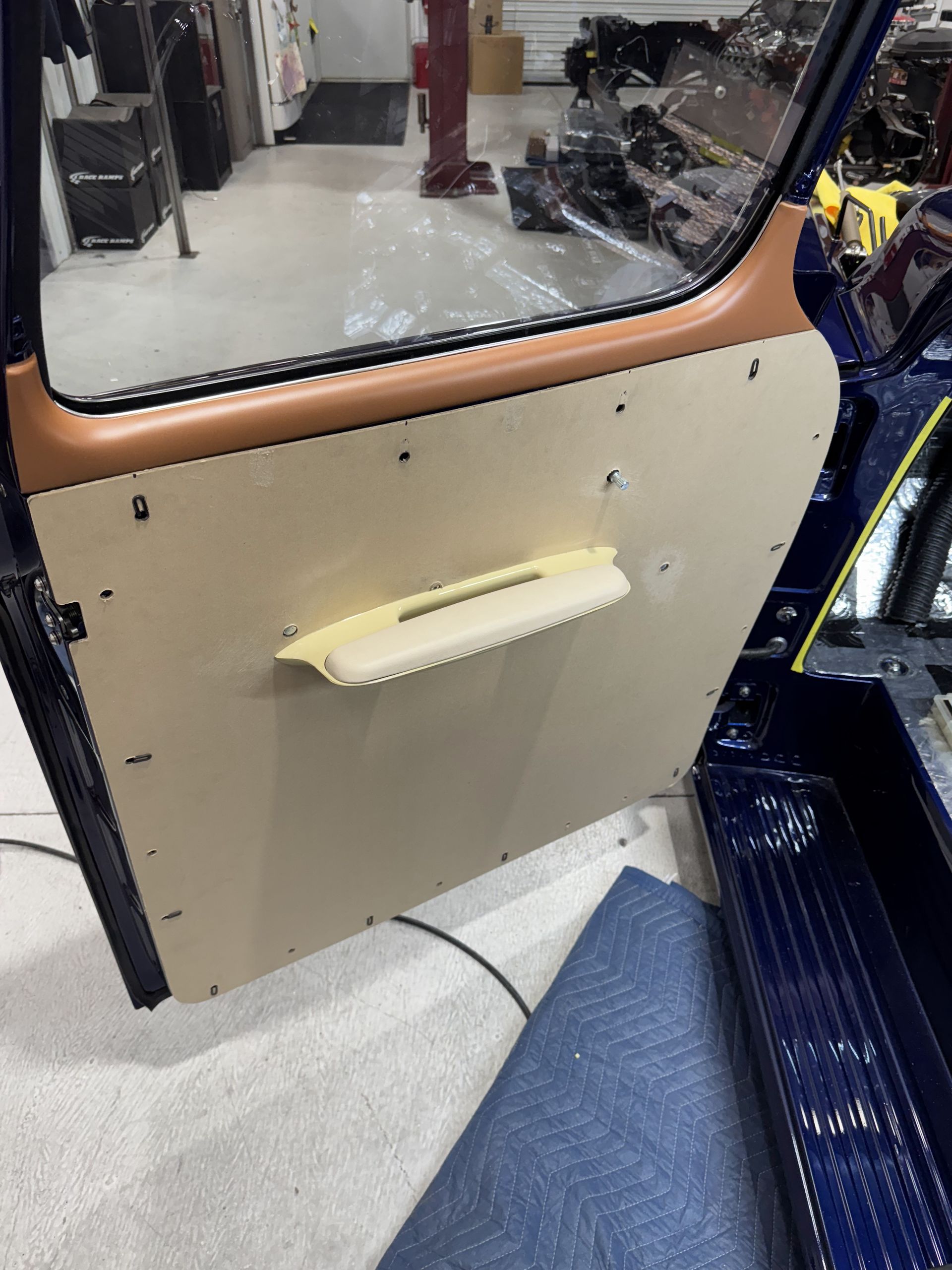 Vehicle door panel with beige armrest and window, viewed inside a shop or garage.