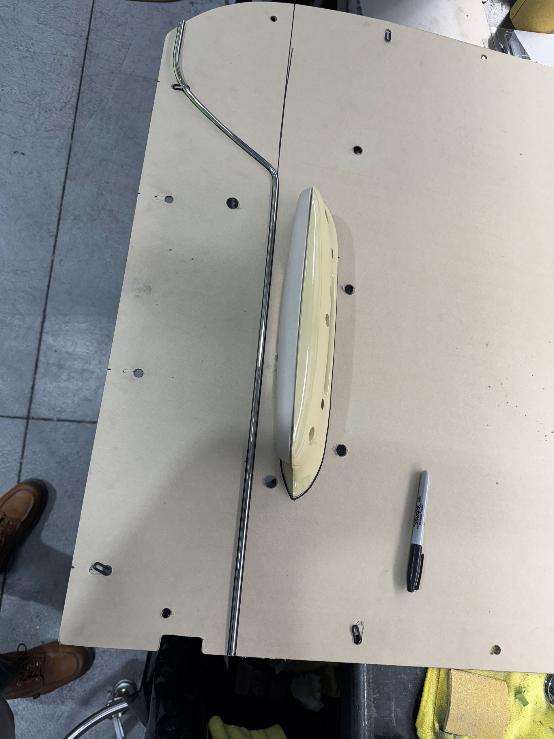 Top-down view of a large white board with a central oval object and a small tool beside it on a tiled floor.