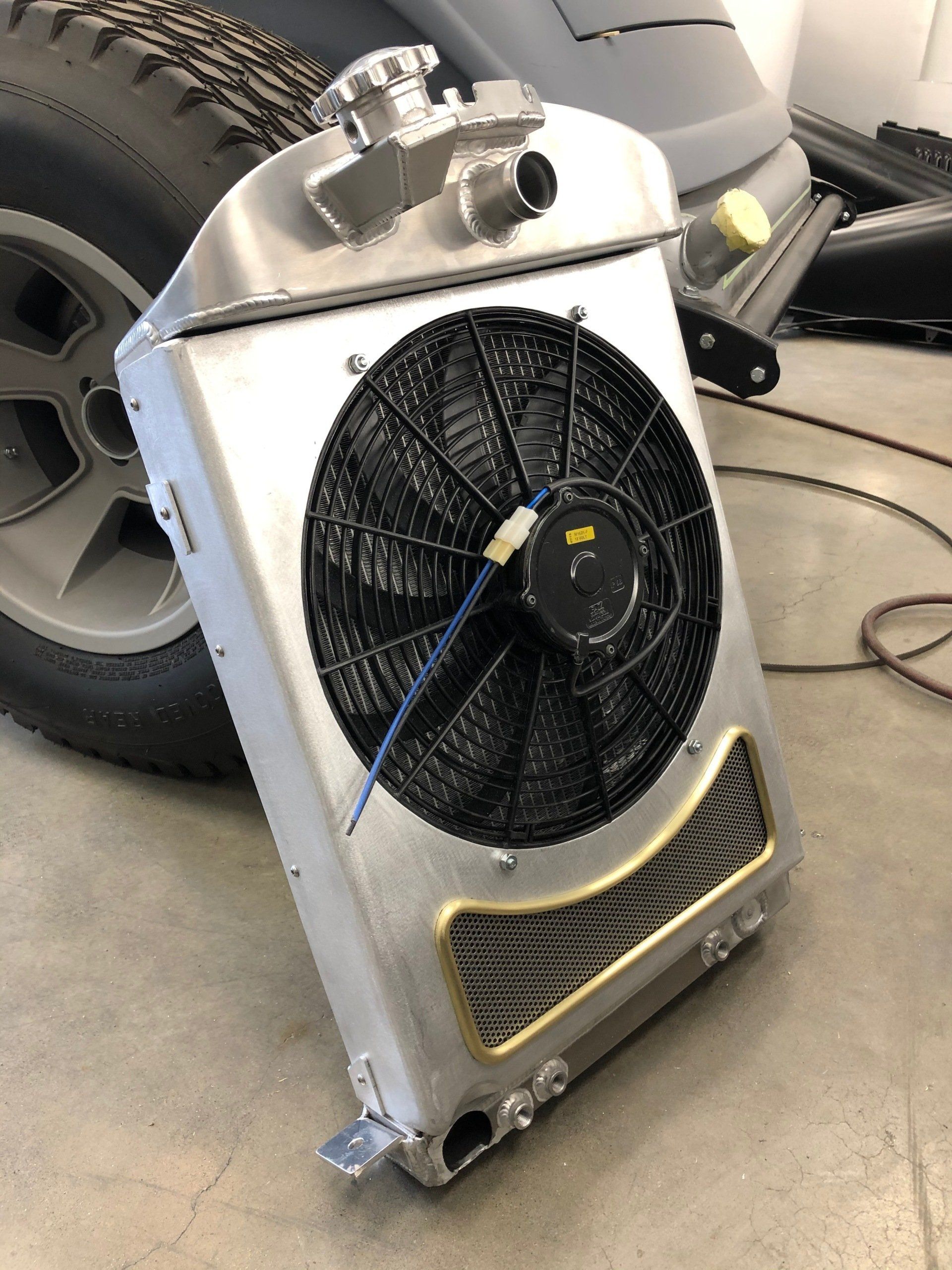 Portable aluminum machine with fan and grille, leaning against a large vehicle tire in a garage