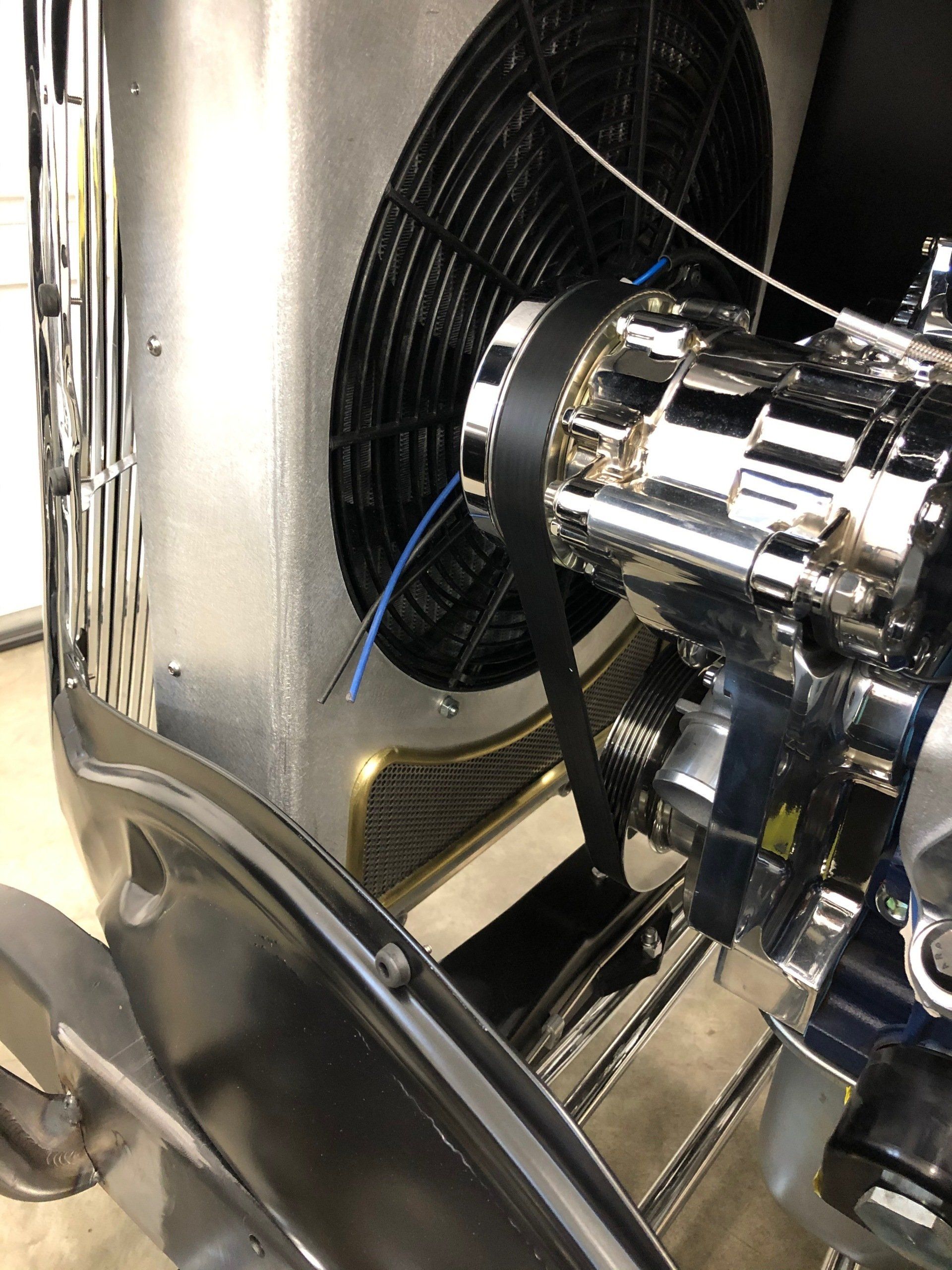 Close-up of chrome engine machinery with black hoses and a fan inside a metallic compartment