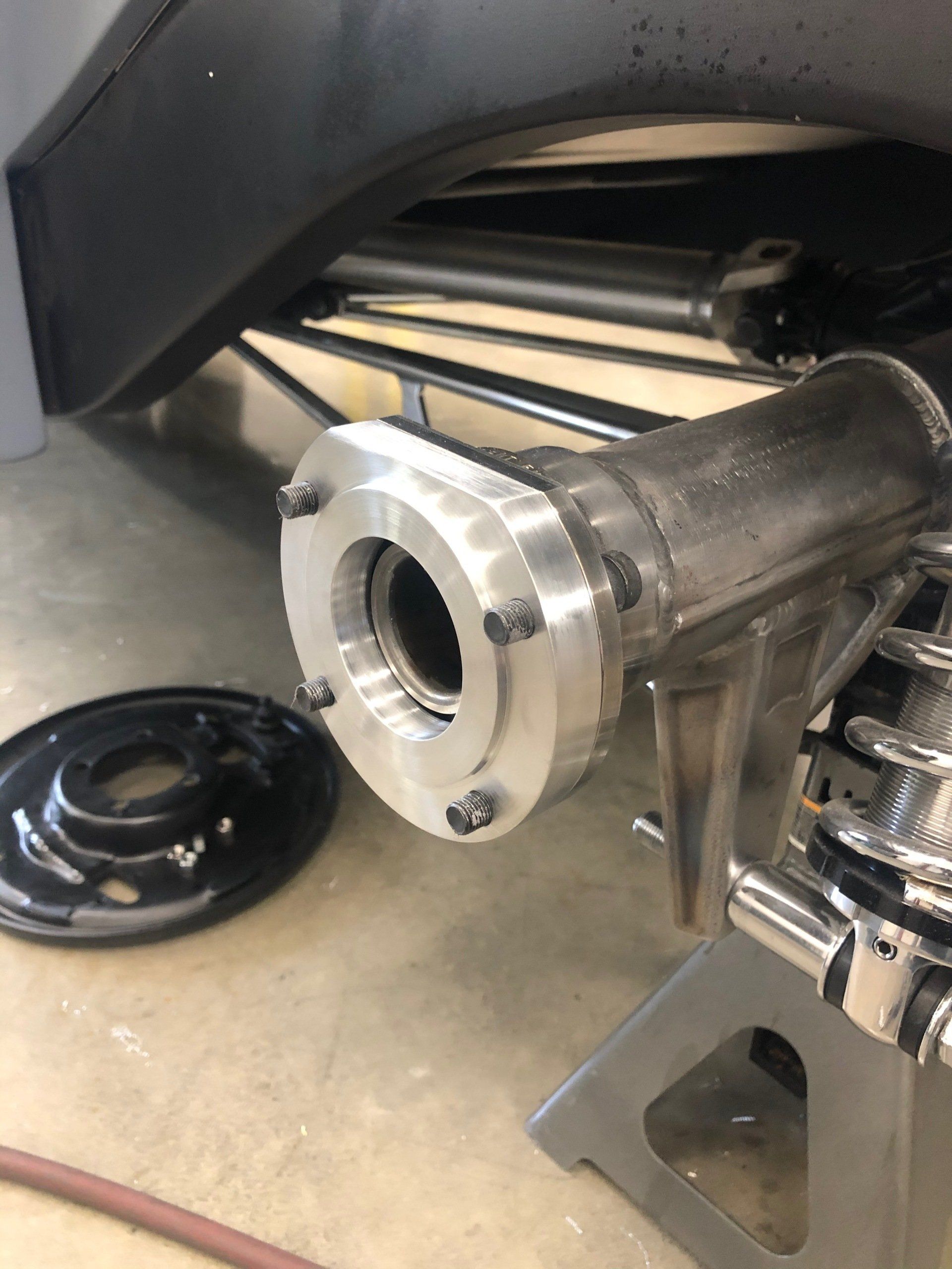 Detached metal motorcycle wheel hub resting on a garage floor next to a black hub cap and a vehicle wheel well