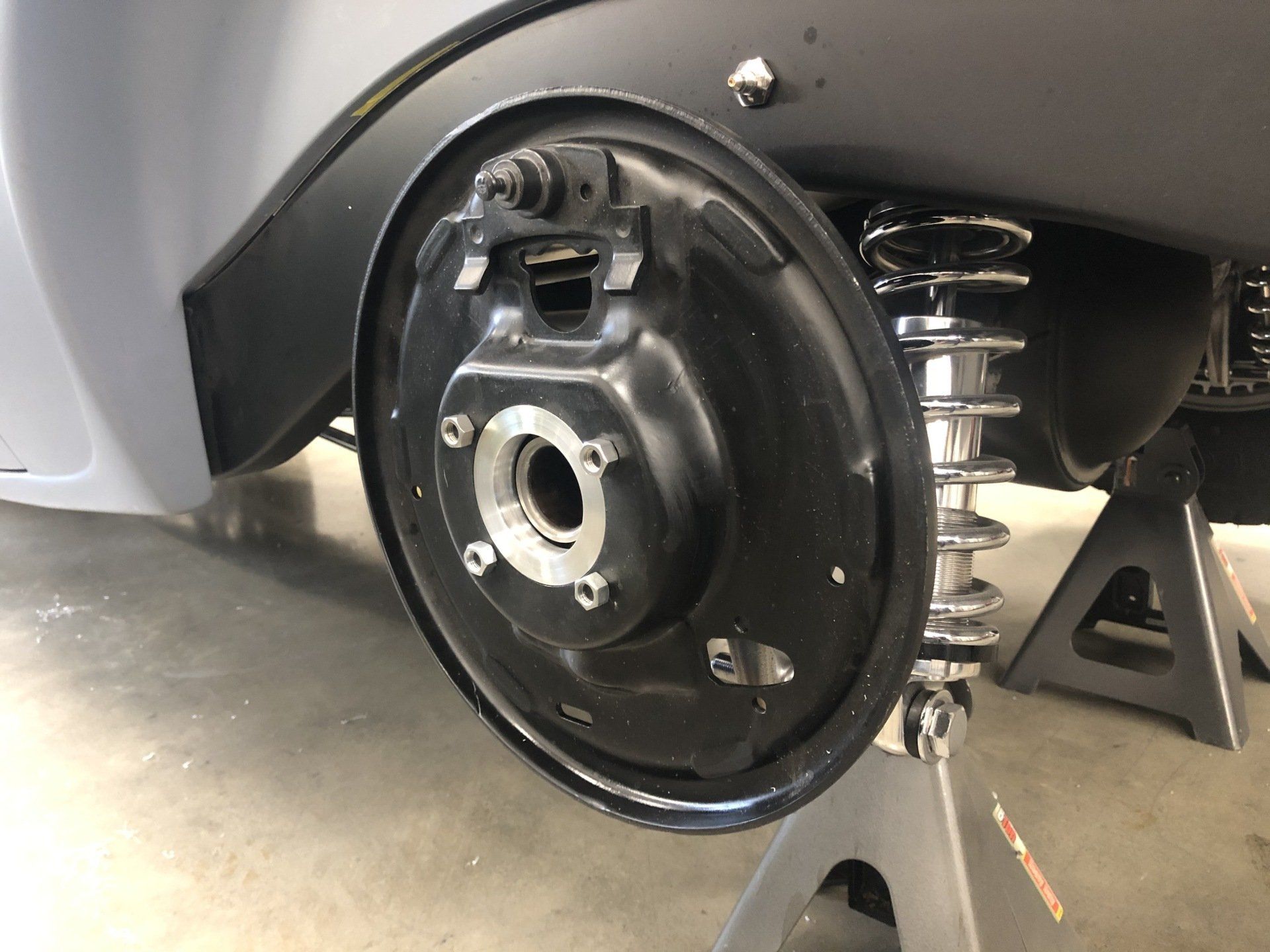 Close-up of a scooter’s rear wheel and brake assembly with exposed suspension in a garage.