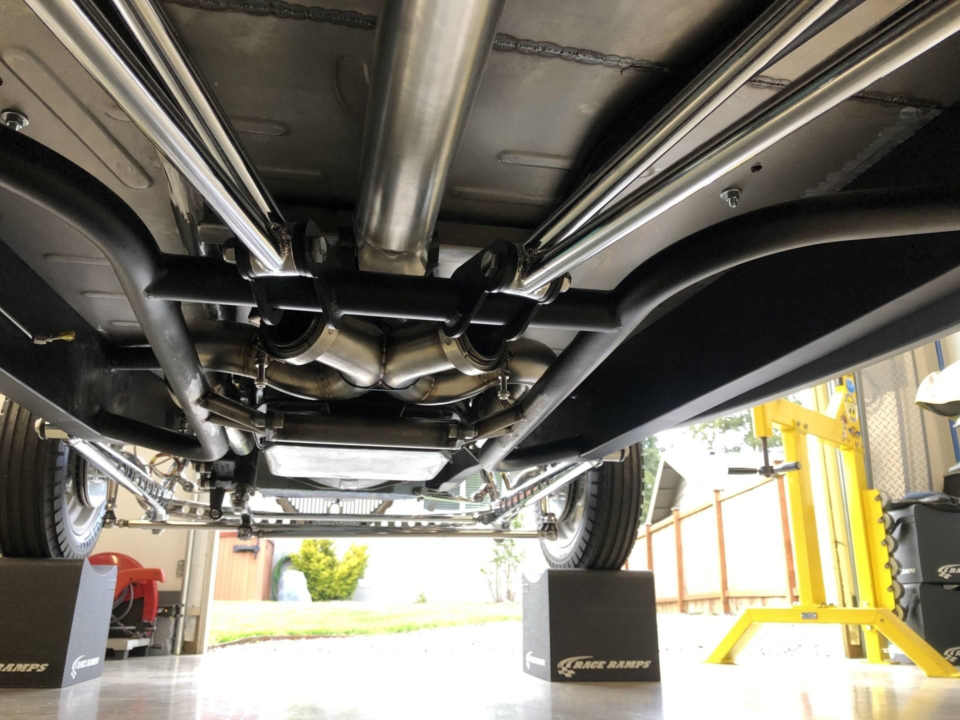 Undercarriage of a car on a lift in a garage, showing exhaust, suspension, and wheels.