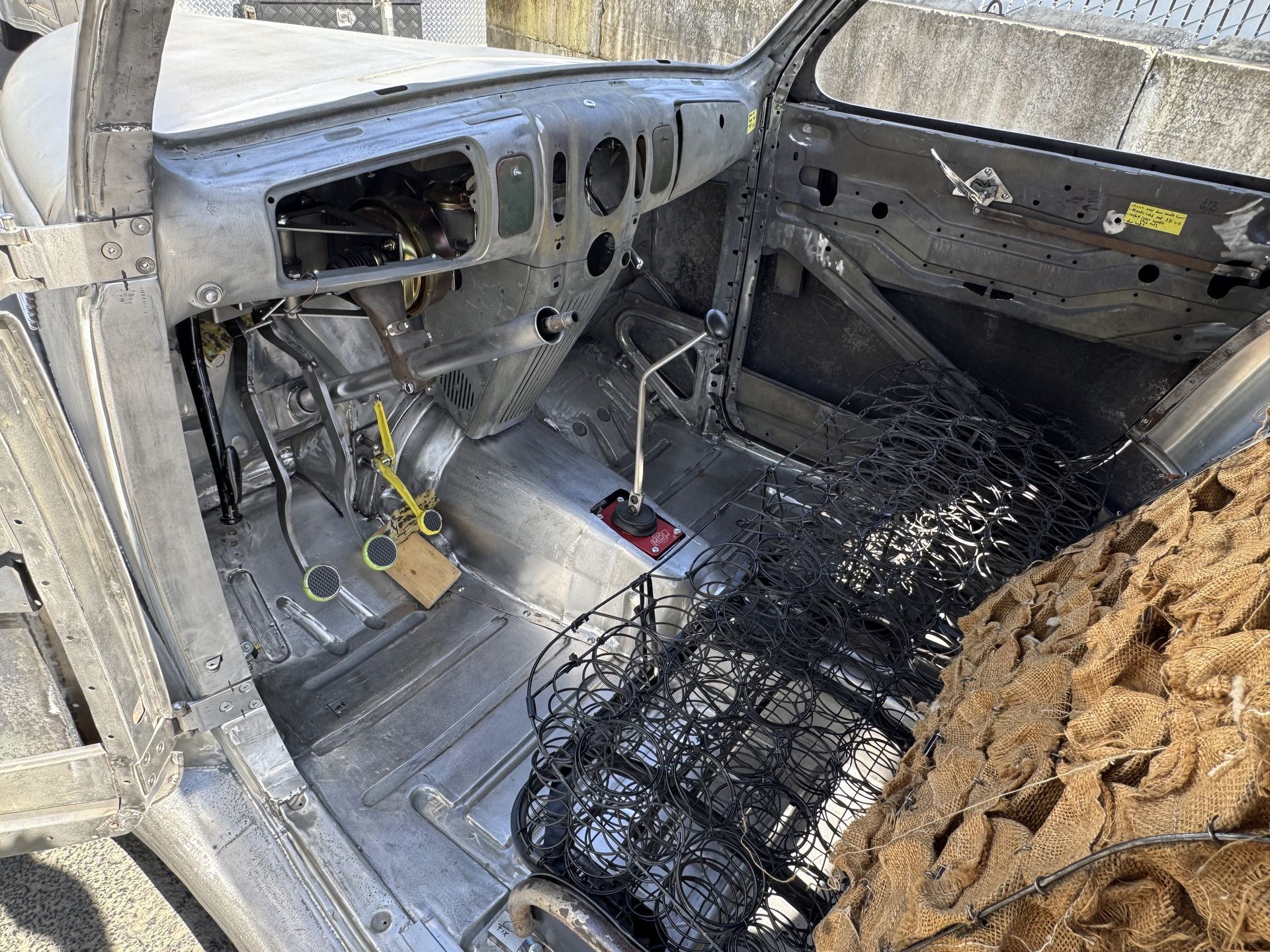 Stripped car interior with exposed metal frame, removed dashboard, and a caged seat area.