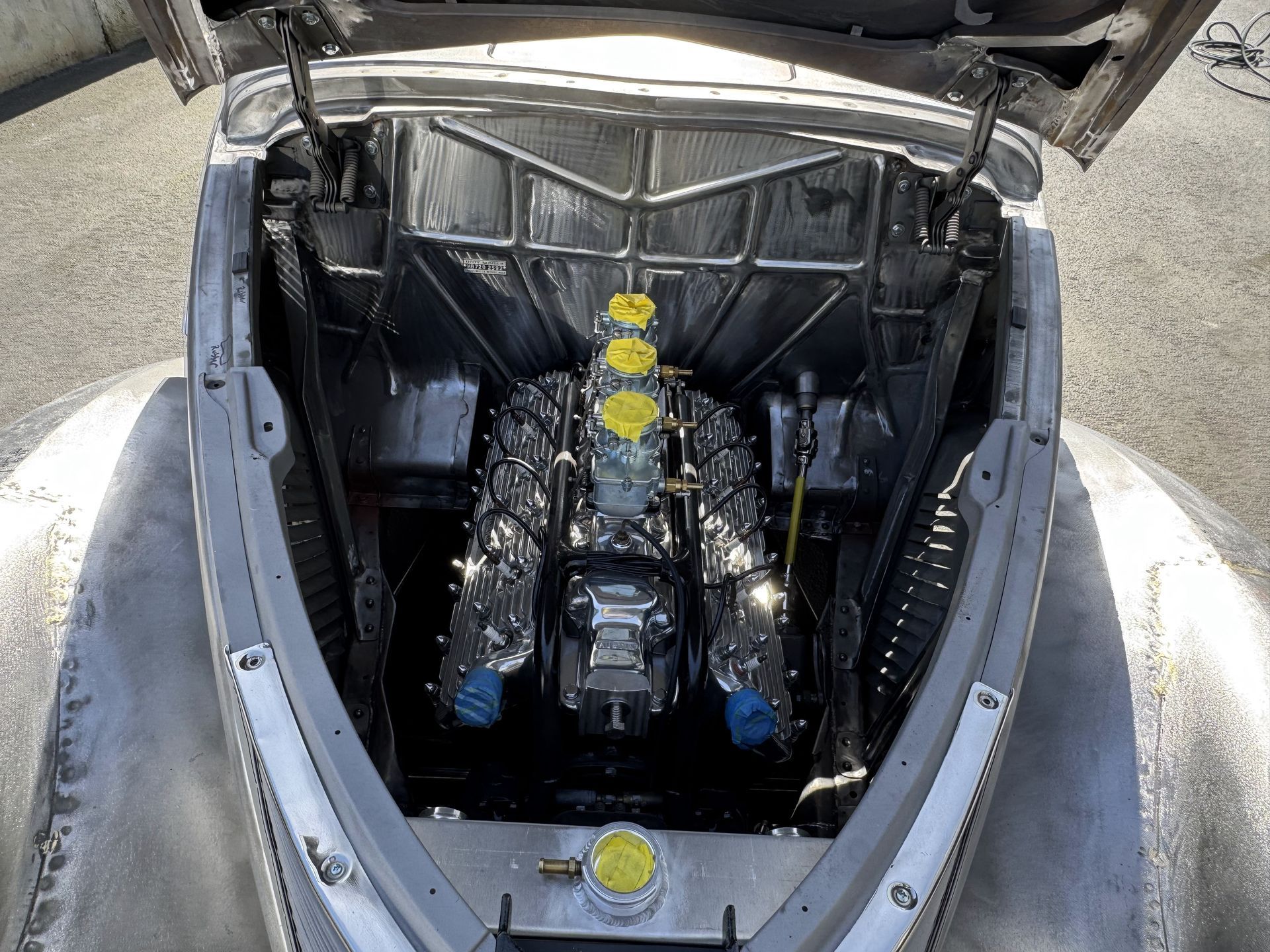 Open car engine bay with black insulation and yellow caps, viewed from above.