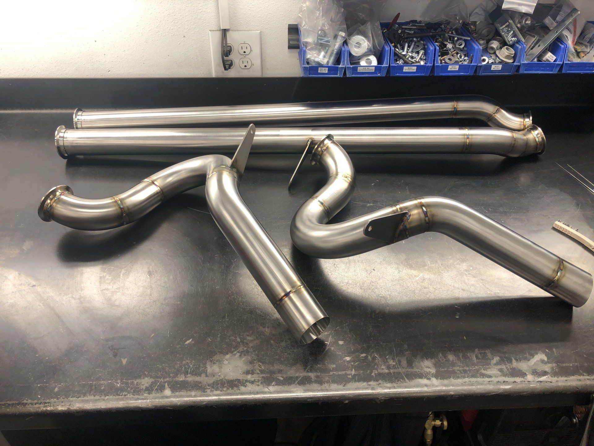 Stainless steel exhaust pipes and tubing laid out on a workbench in a workshop.
