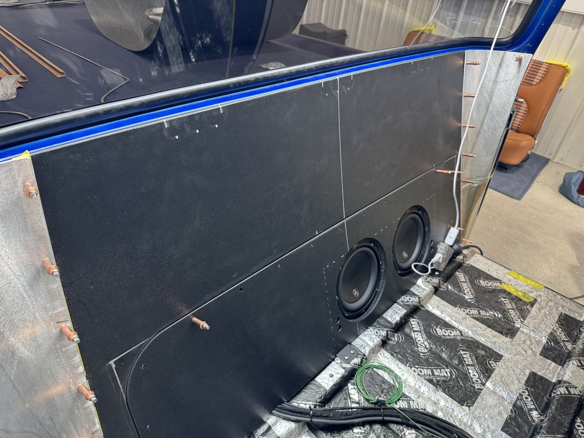 Large black speaker cabinet with two subwoofers, wrapped in blue tape and leaning on a carpeted floor.