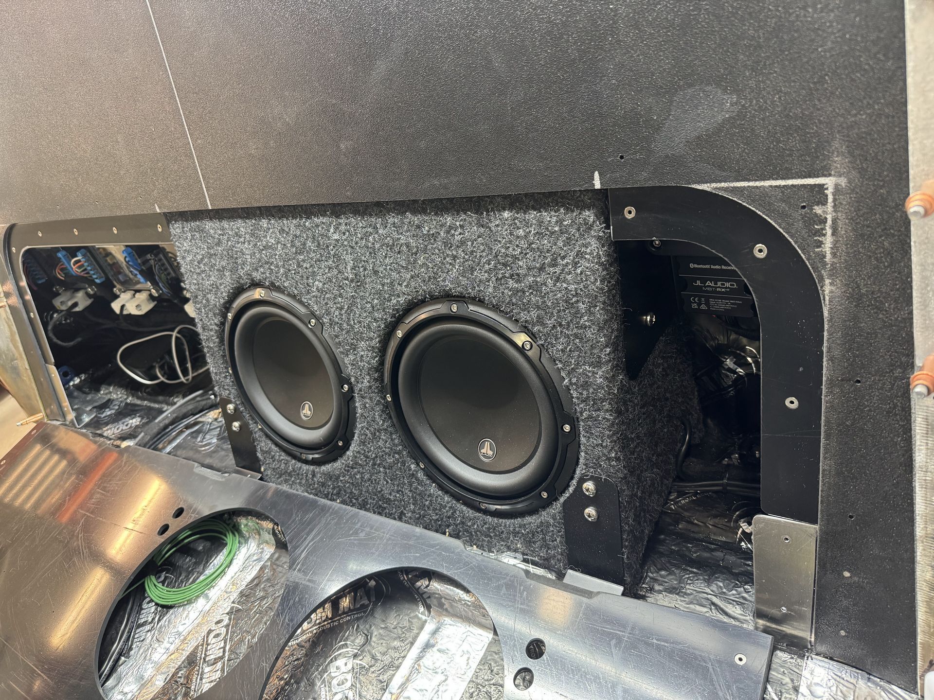 Black speaker enclosure with two round subwoofers mounted in a car trunk.