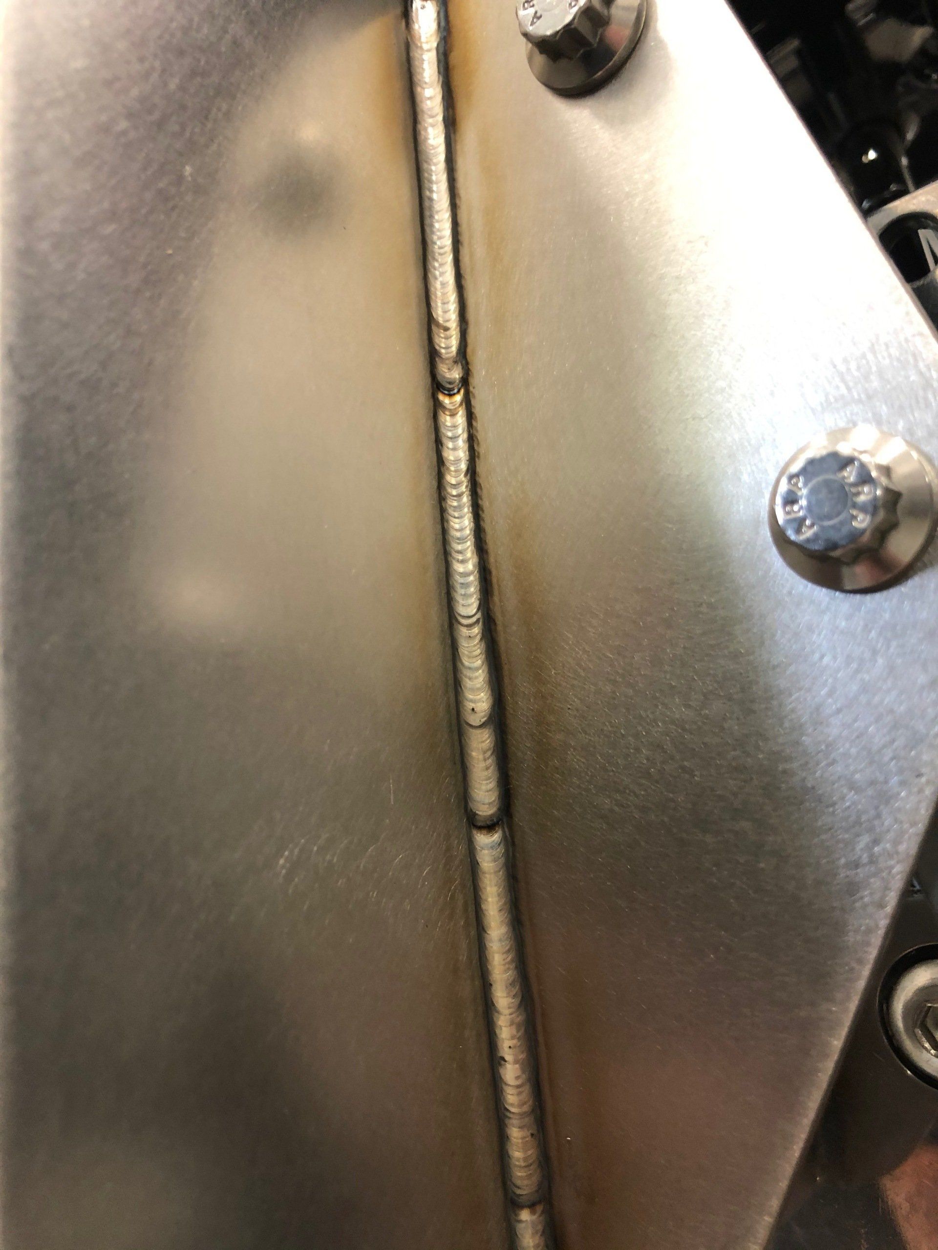 Close-up of a metal hinge with screws on a silver surface.