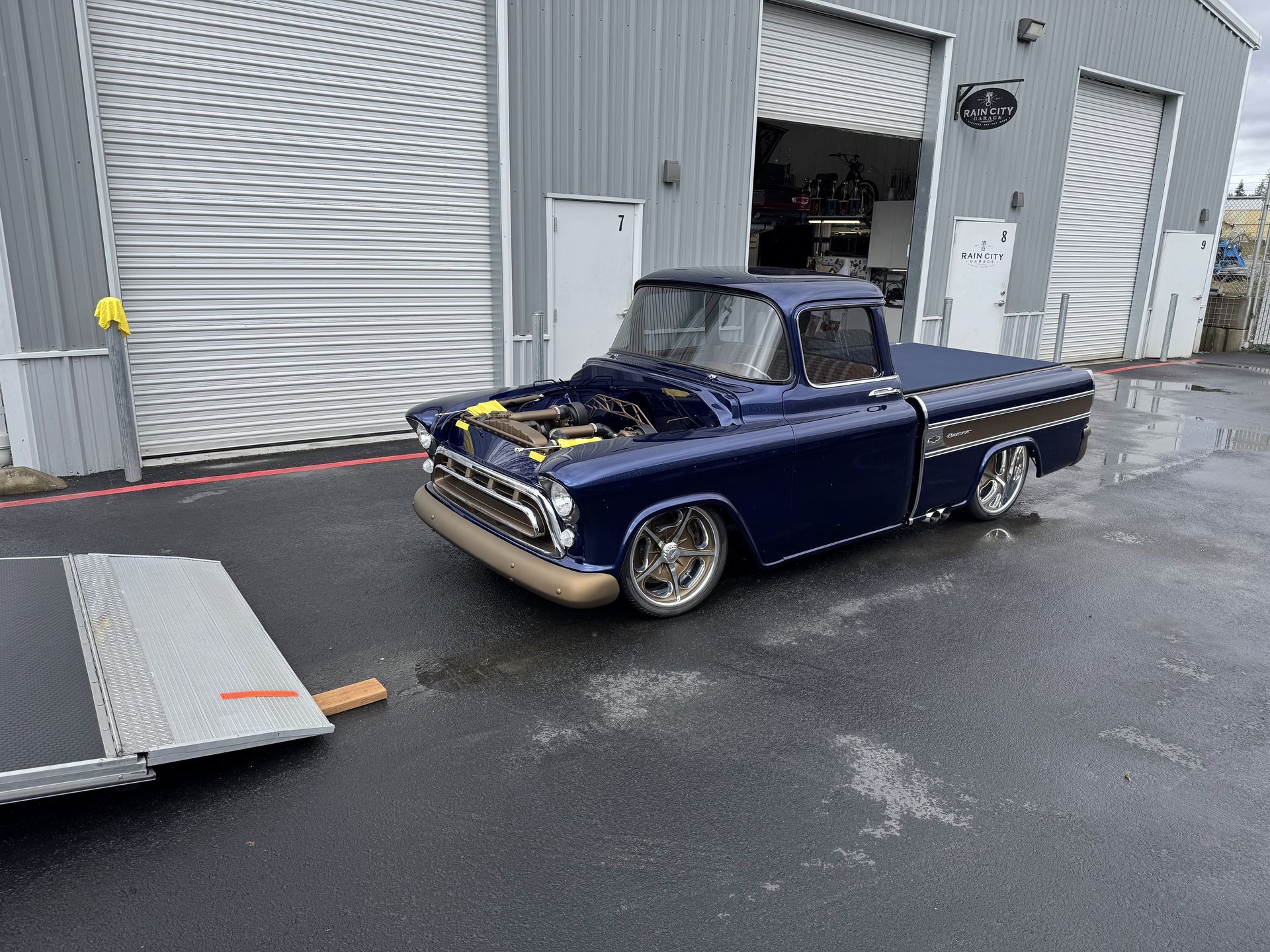 Lowered blue vintage pickup truck parked outside a garage on wet pavement