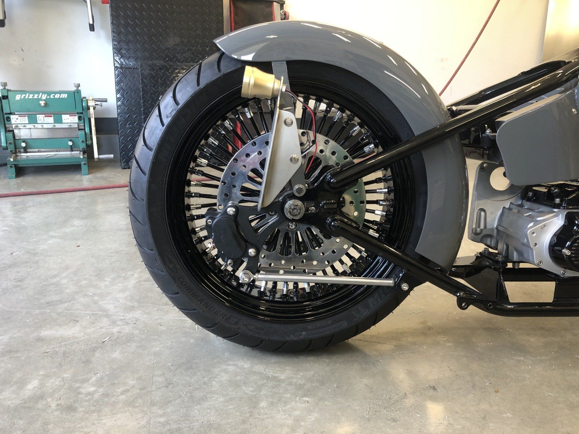 Black custom motorcycle rear wheel and suspension in a garage.