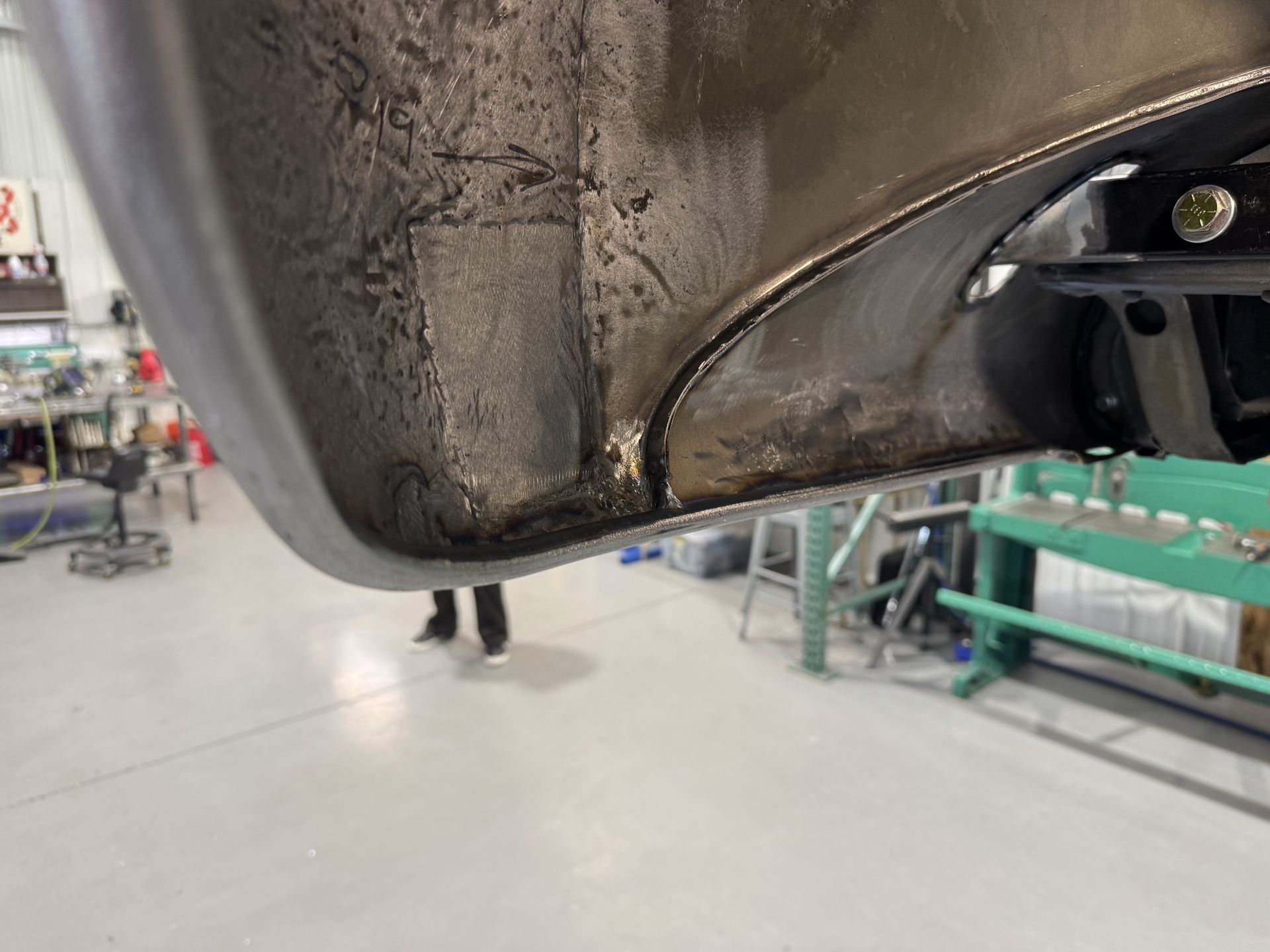 Close-up of a dirty car bumper with black grime and a tow hitch, in a garage.