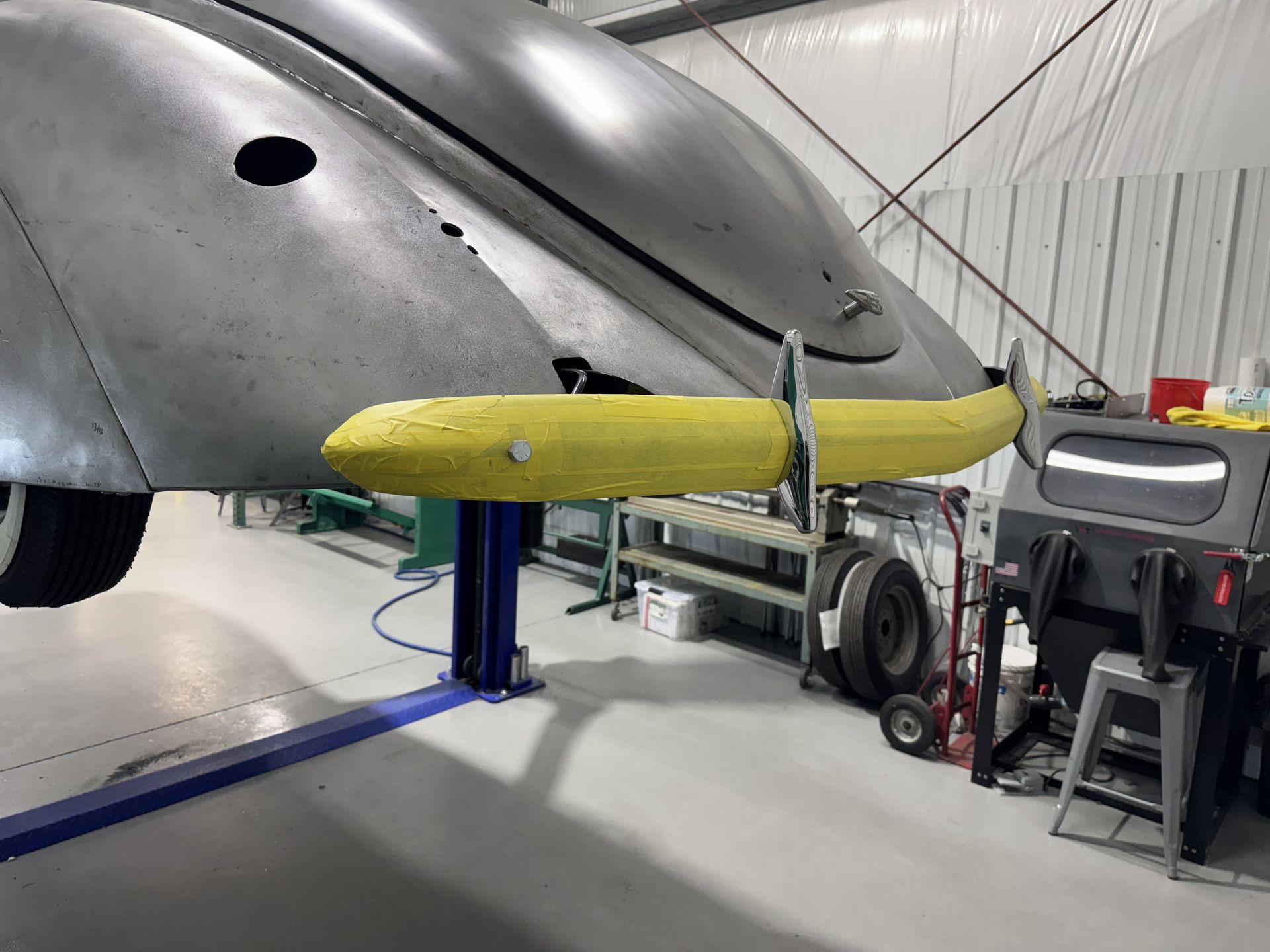 Yellow propeller mounted on a silver aircraft in a hangar with maintenance equipment nearby