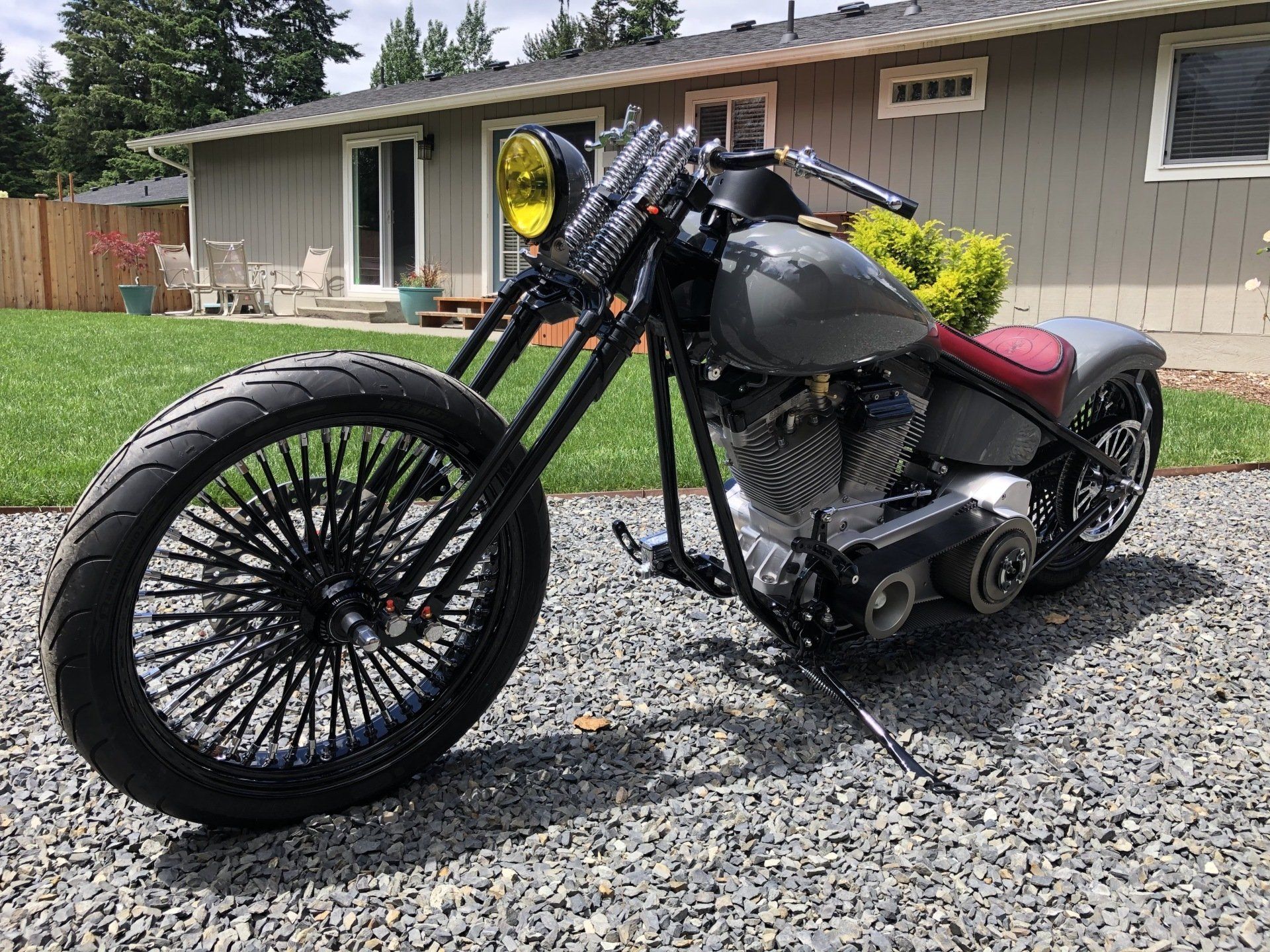 Black custom chopper motorcycle parked on gravel in front of a gray house.