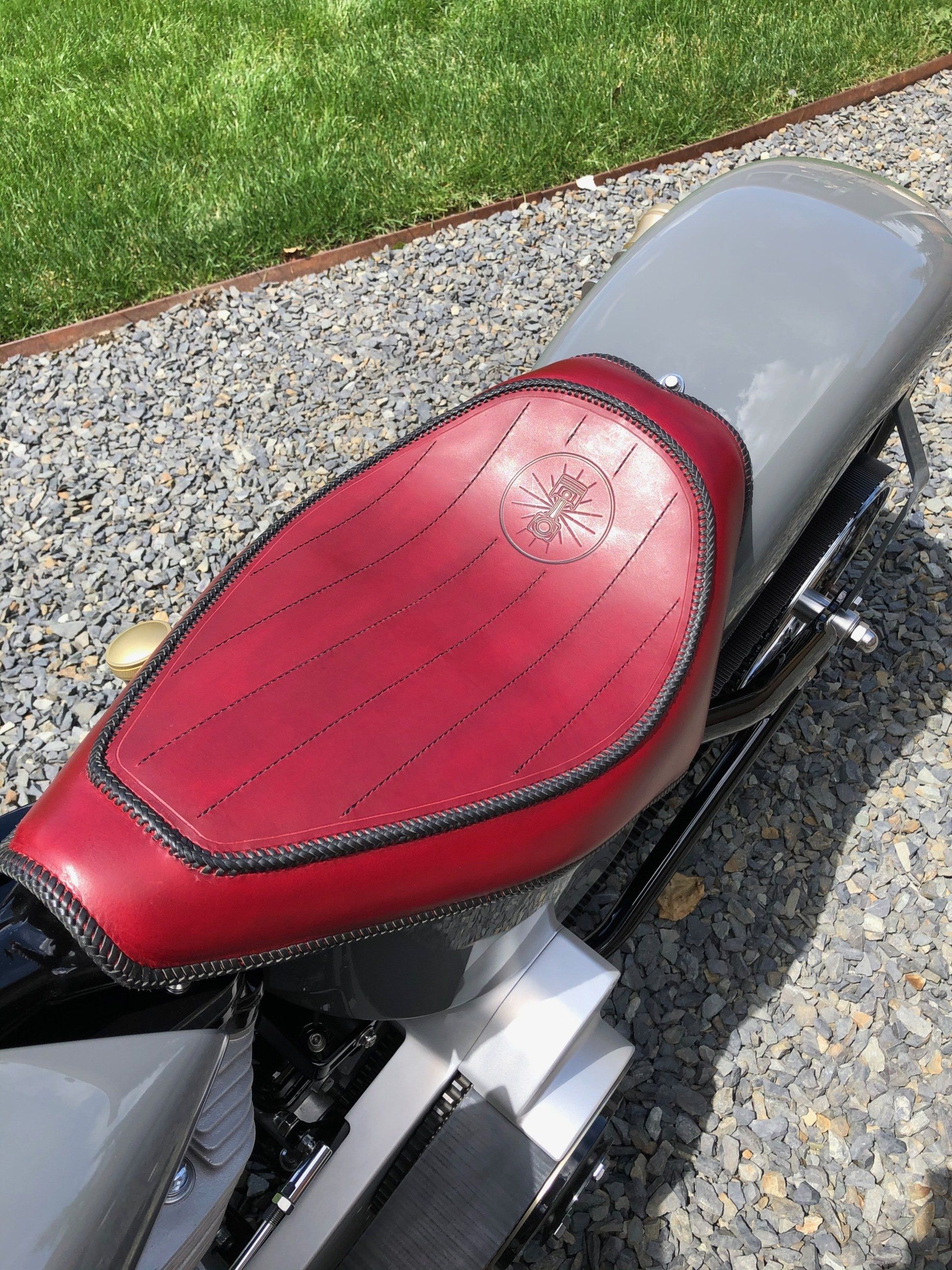 Red motorcycle seat on a gravel path beside grass.
