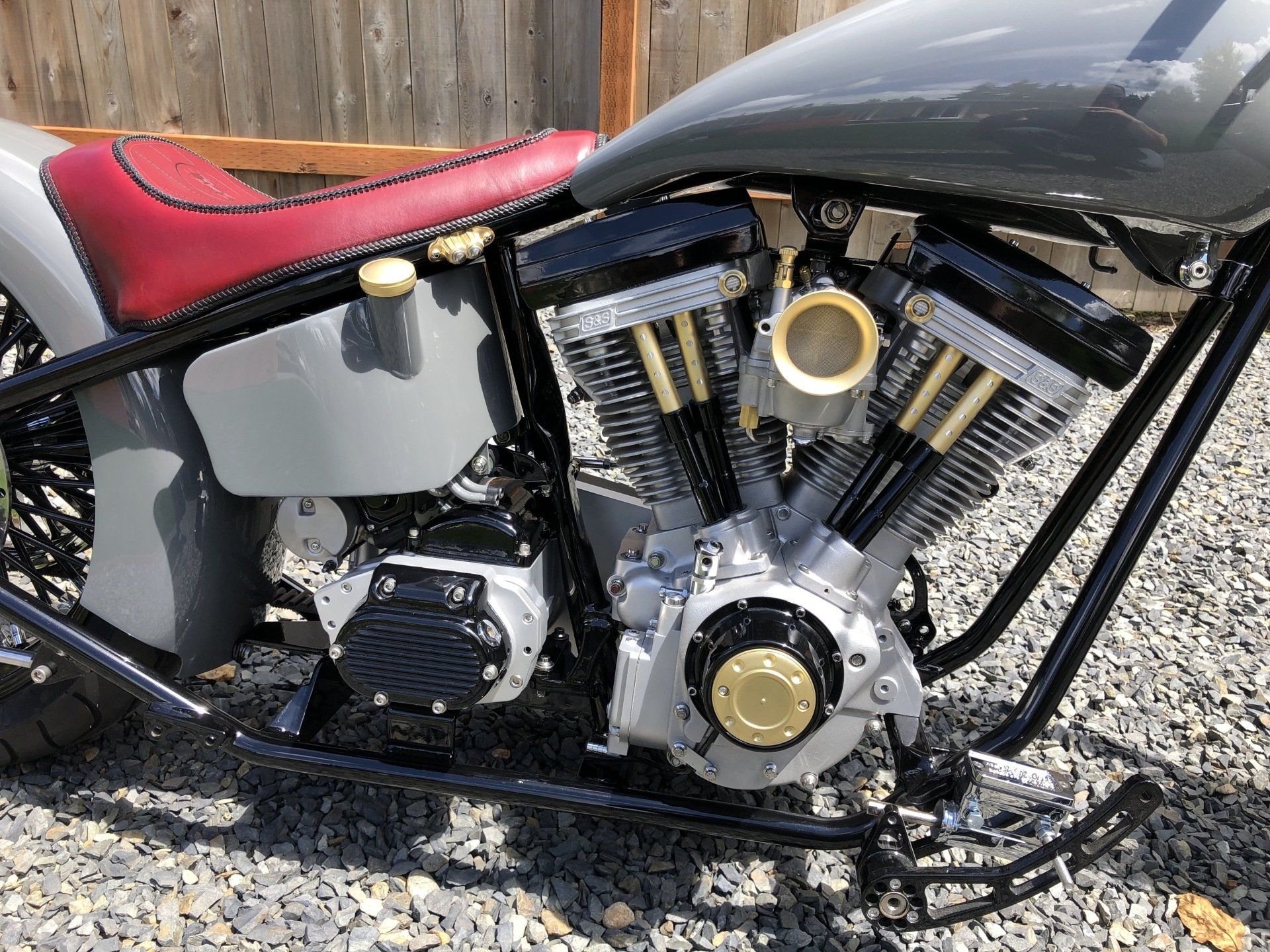 Custom motorcycle with red seat, black frame, and exposed engine parked on gravel.