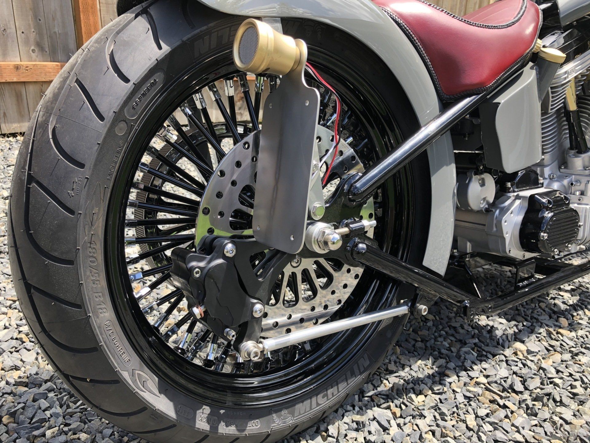 Custom black motorcycle rear wheel with gold accents and red seat on gravel road
