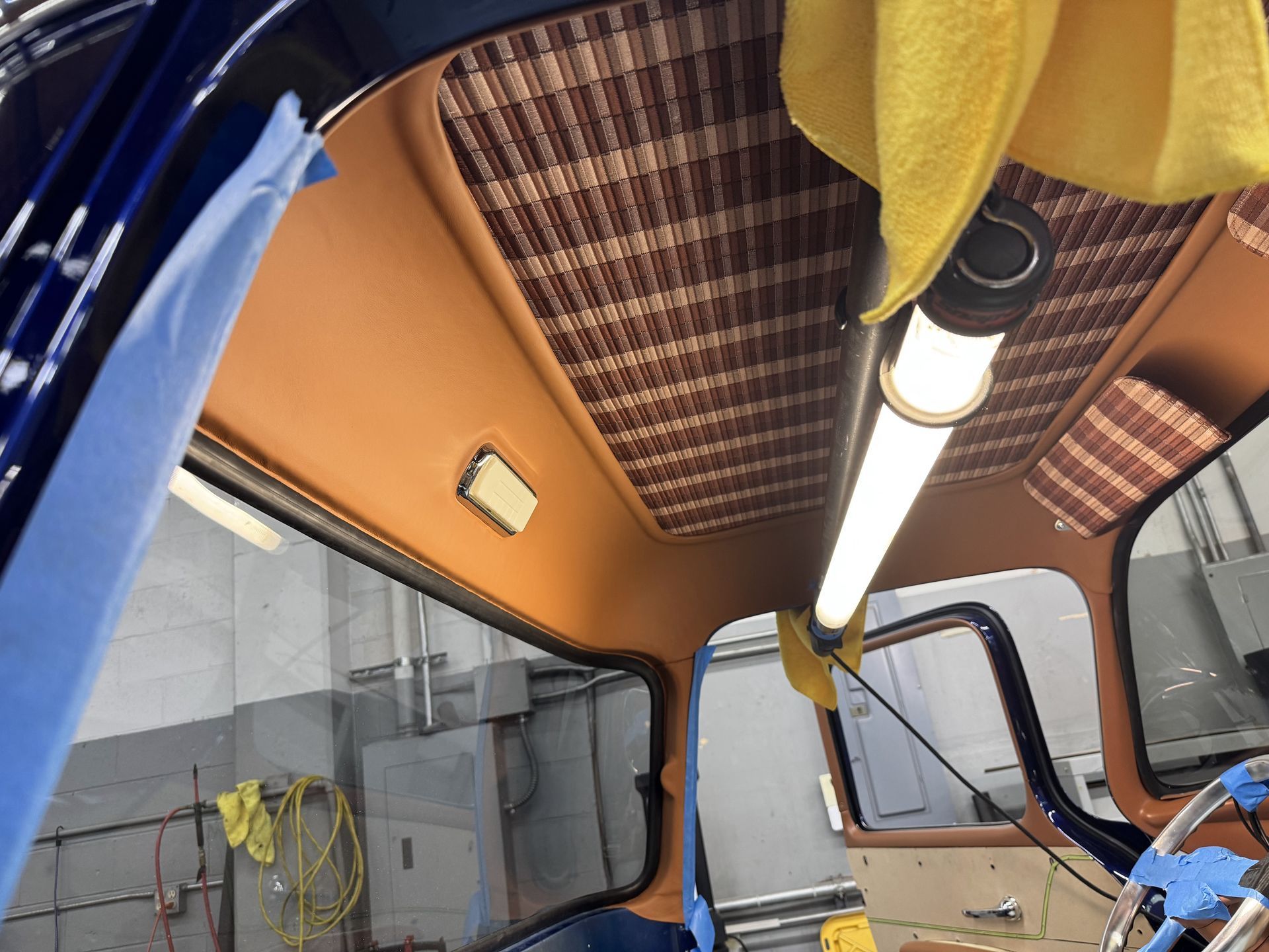 Inside a vehicle cab with orange ceiling panels, blue frame, and hanging yellow cloth near a light