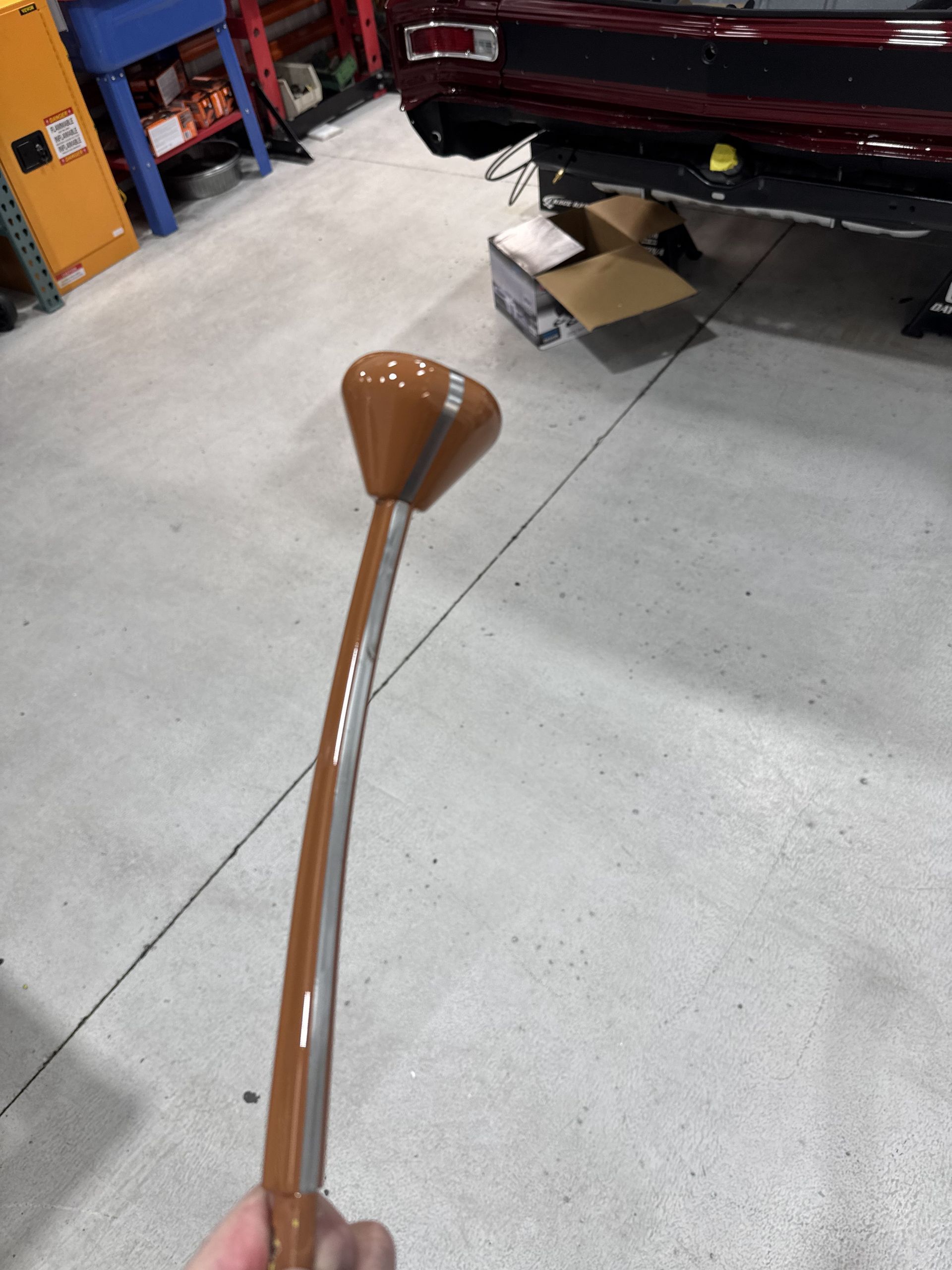 Brown-handled cane with a curved tip on a gray garage floor near boxes and a vehicle.