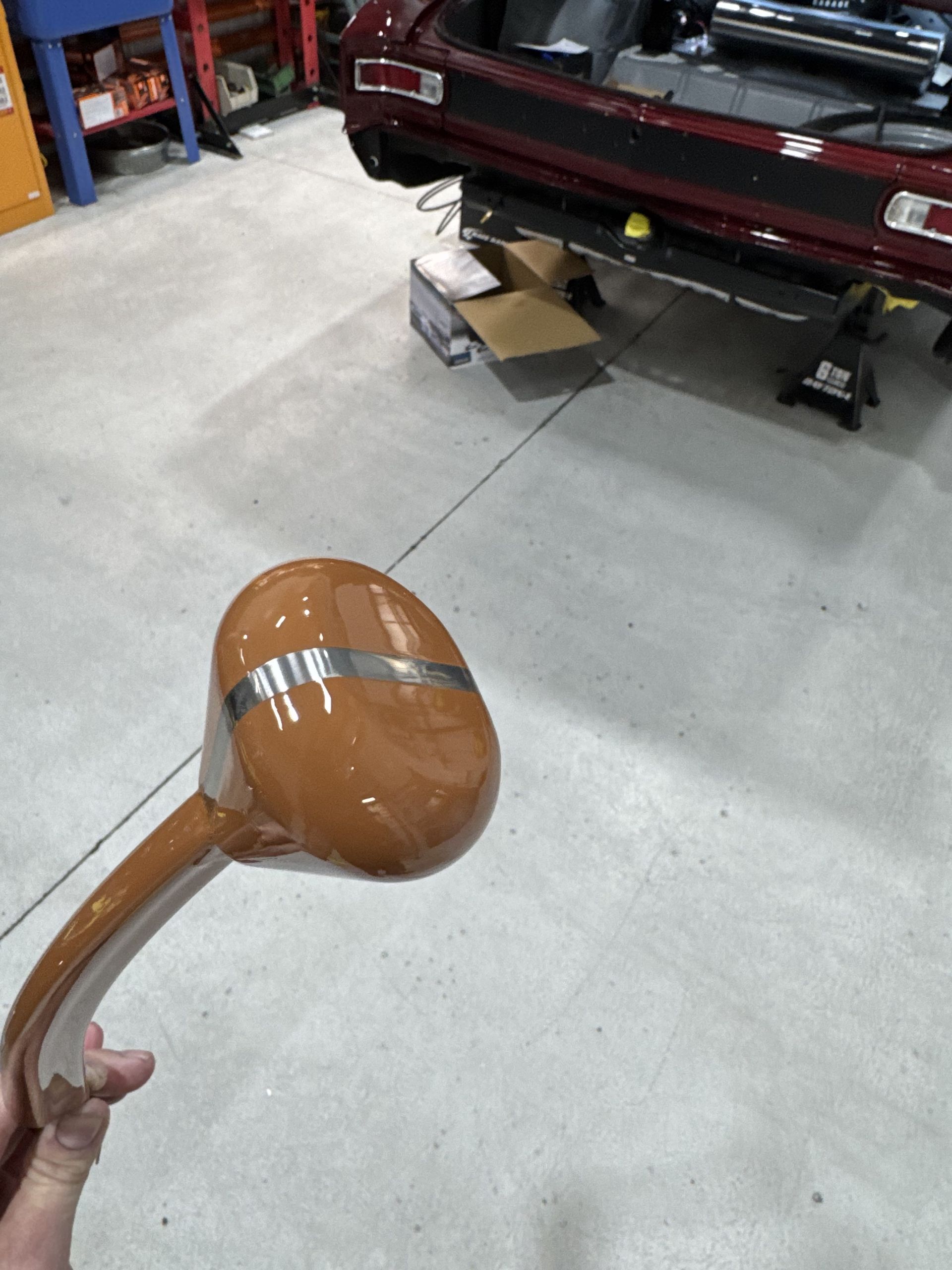 Hand holding a brown painted car side mirror in a garage with a truck in the background
