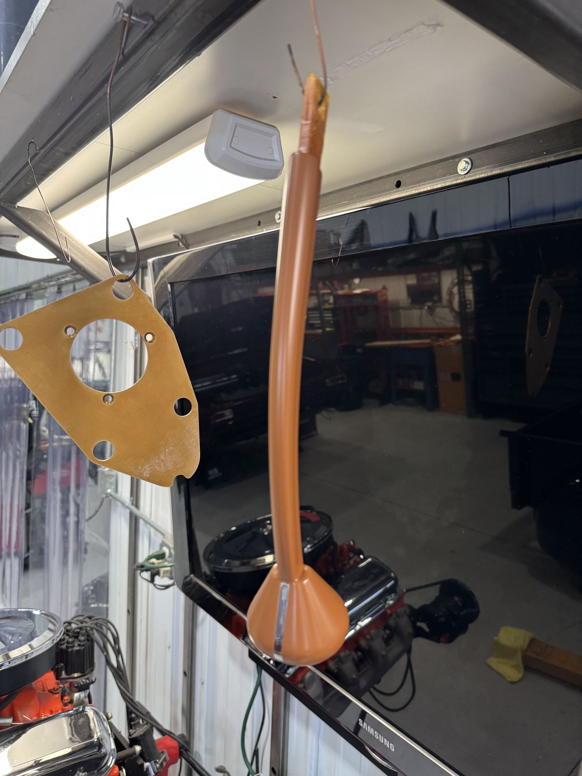 Orange glass pendant hanging in a workshop beside a large dark window and ceiling lights