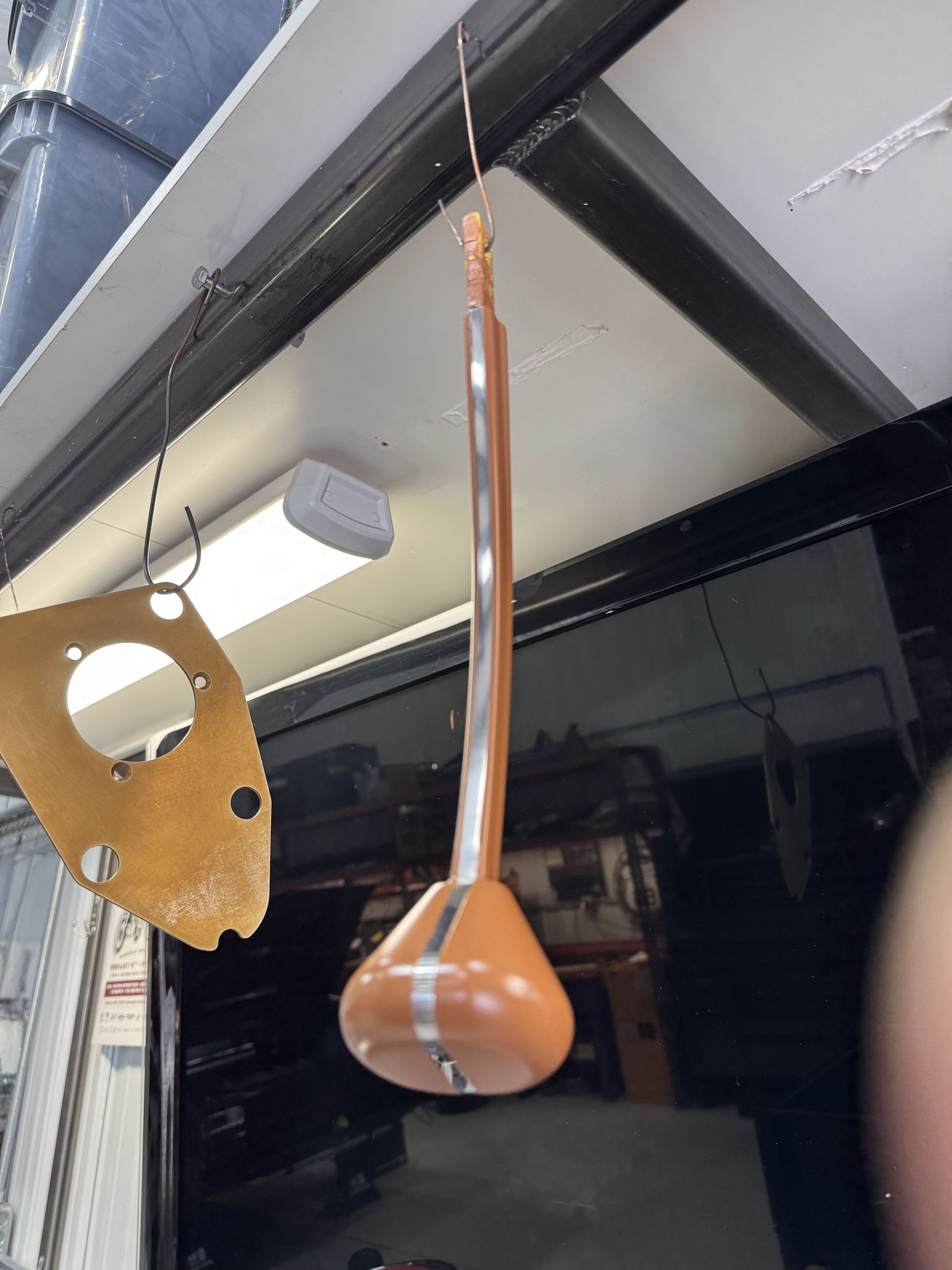 Orange hanging pendant lamp under a ceiling beam in a workshop or garage, beside a wooden object and speaker-like fixture
