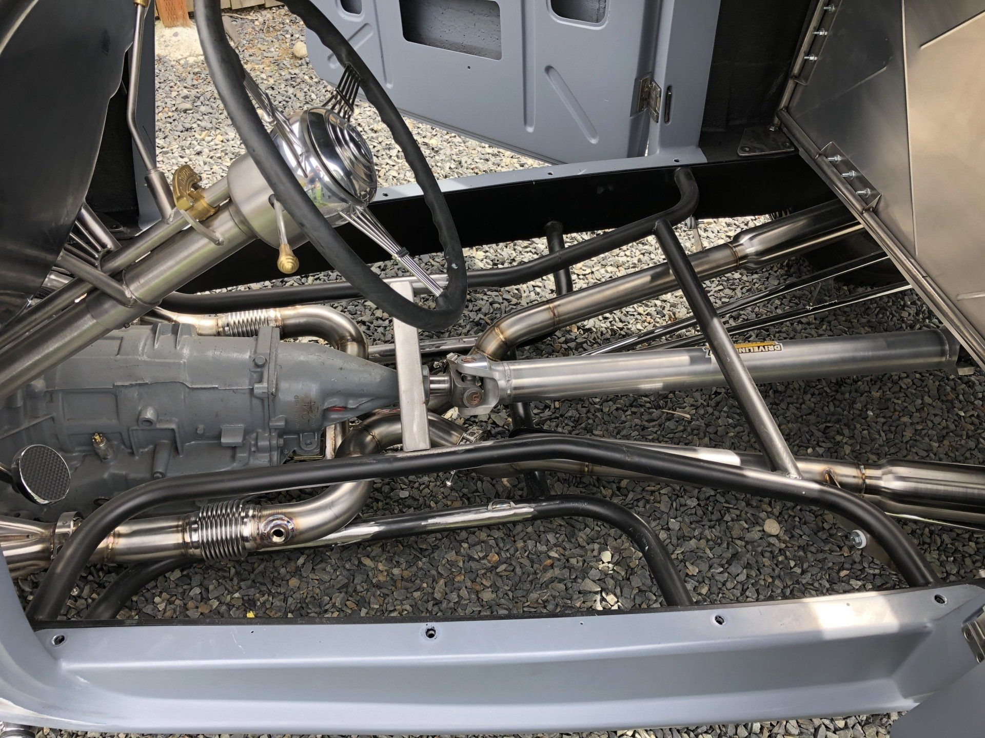Interior of a stripped car chassis with exposed metal frame, steering wheel, and tubing.
