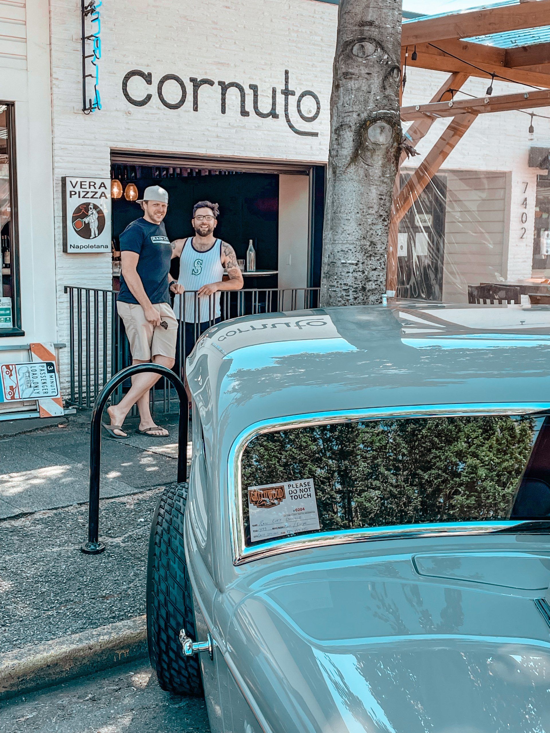 Two people standing outside the Cornuto shop beside a light blue vintage car.