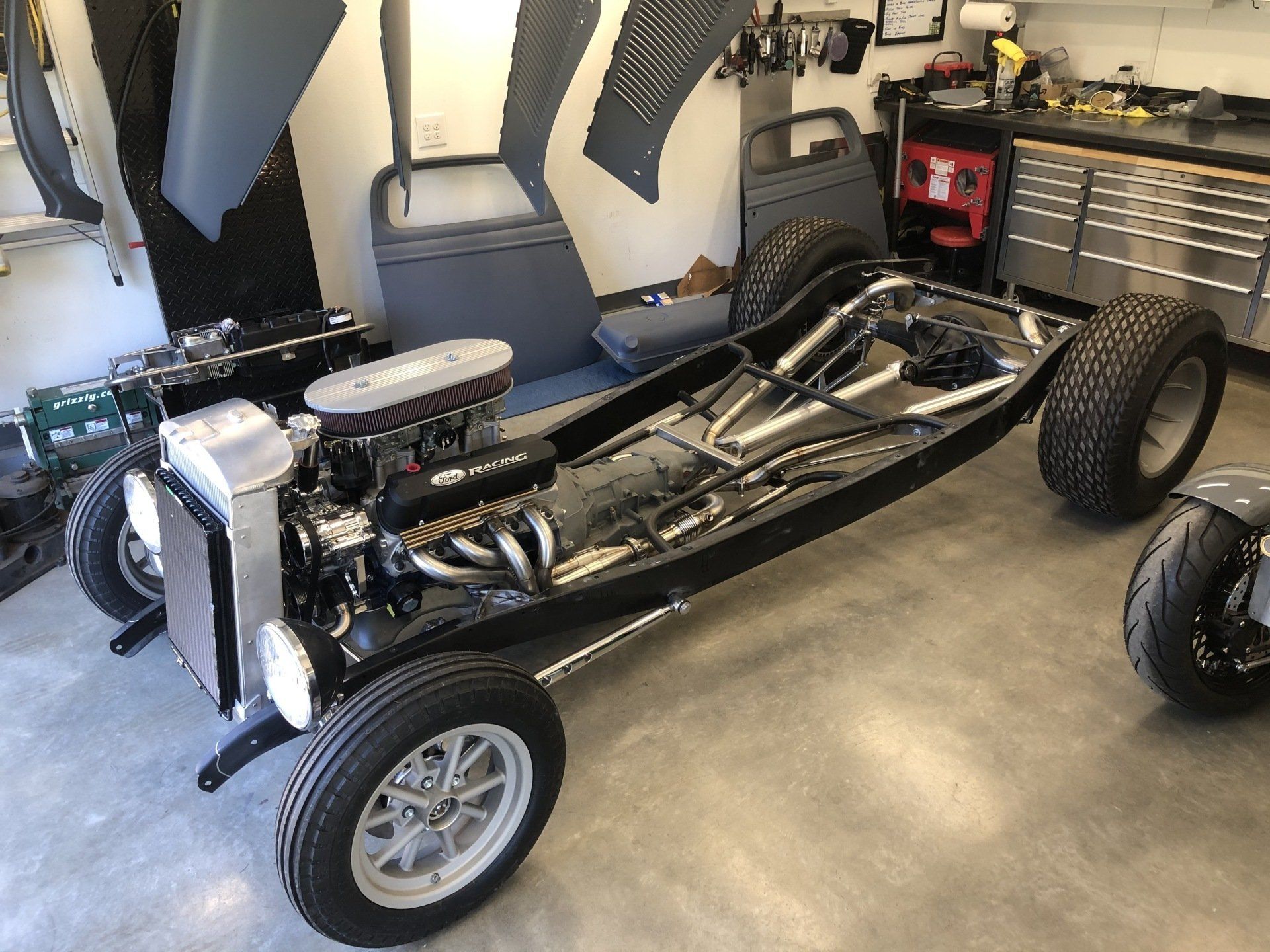 Classic black hot rod chassis in a garage, with exposed engine and body frame on display.