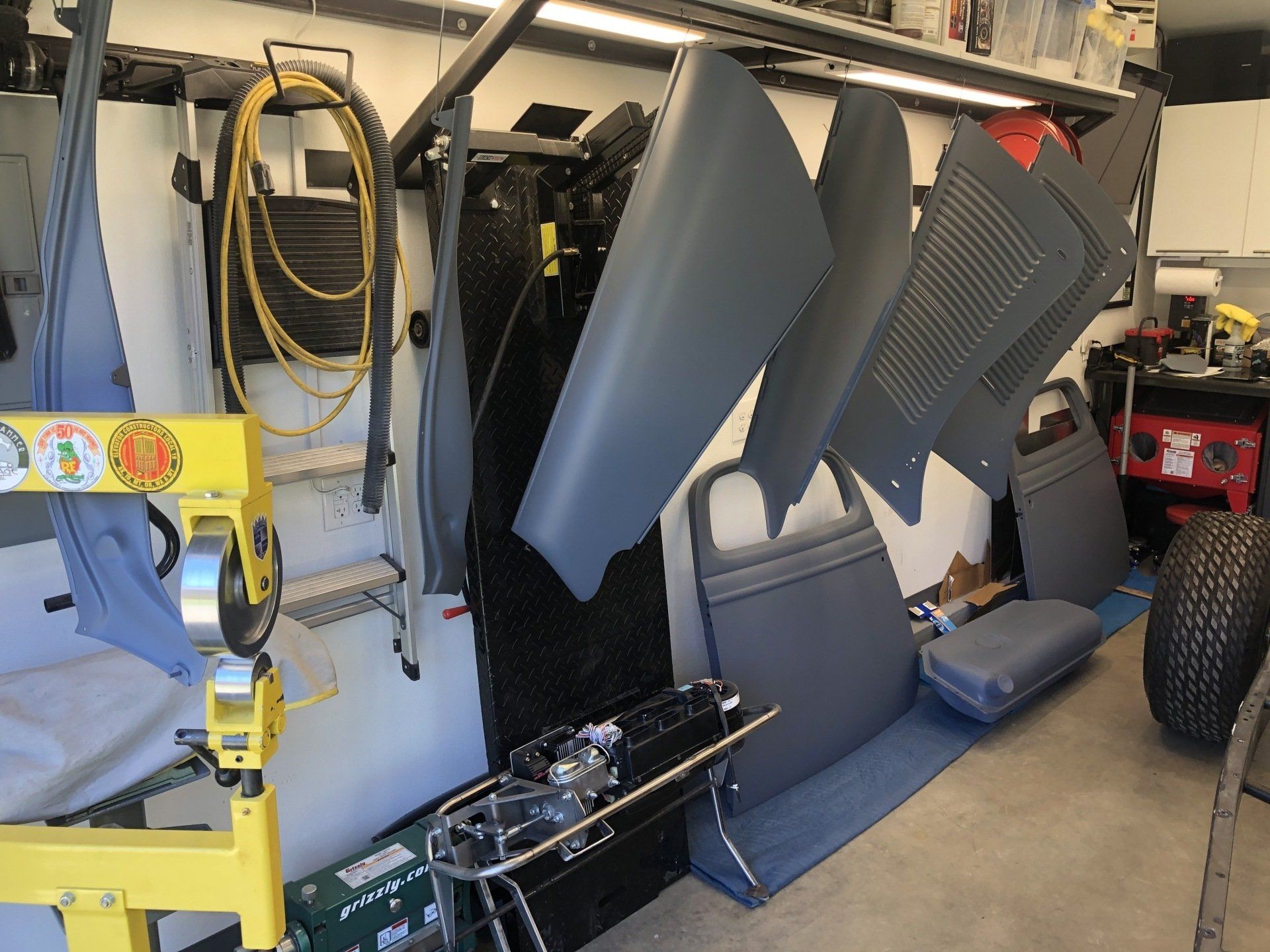 Garage wall with stacked car interior panels and parts, plus yellow equipment and tires in the background