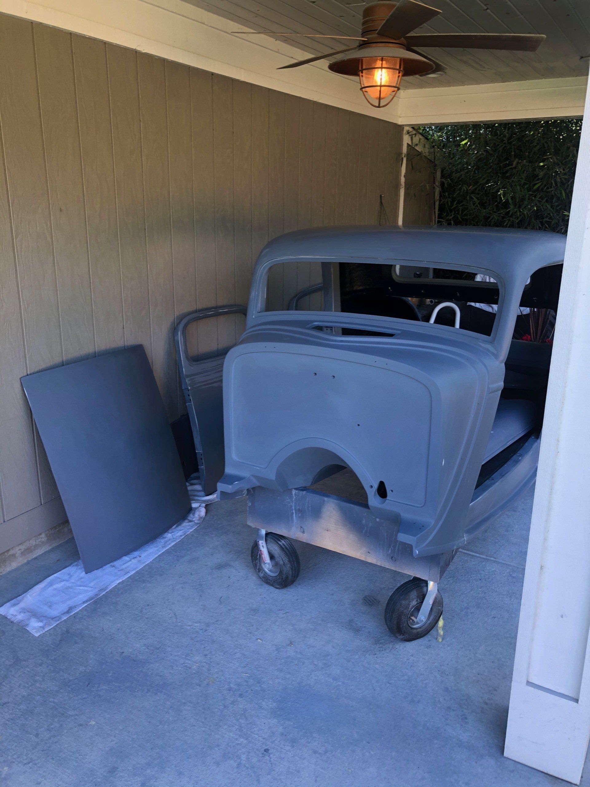 Covered patio with a gray vintage car body on wheels and a leaning panel against the wall.