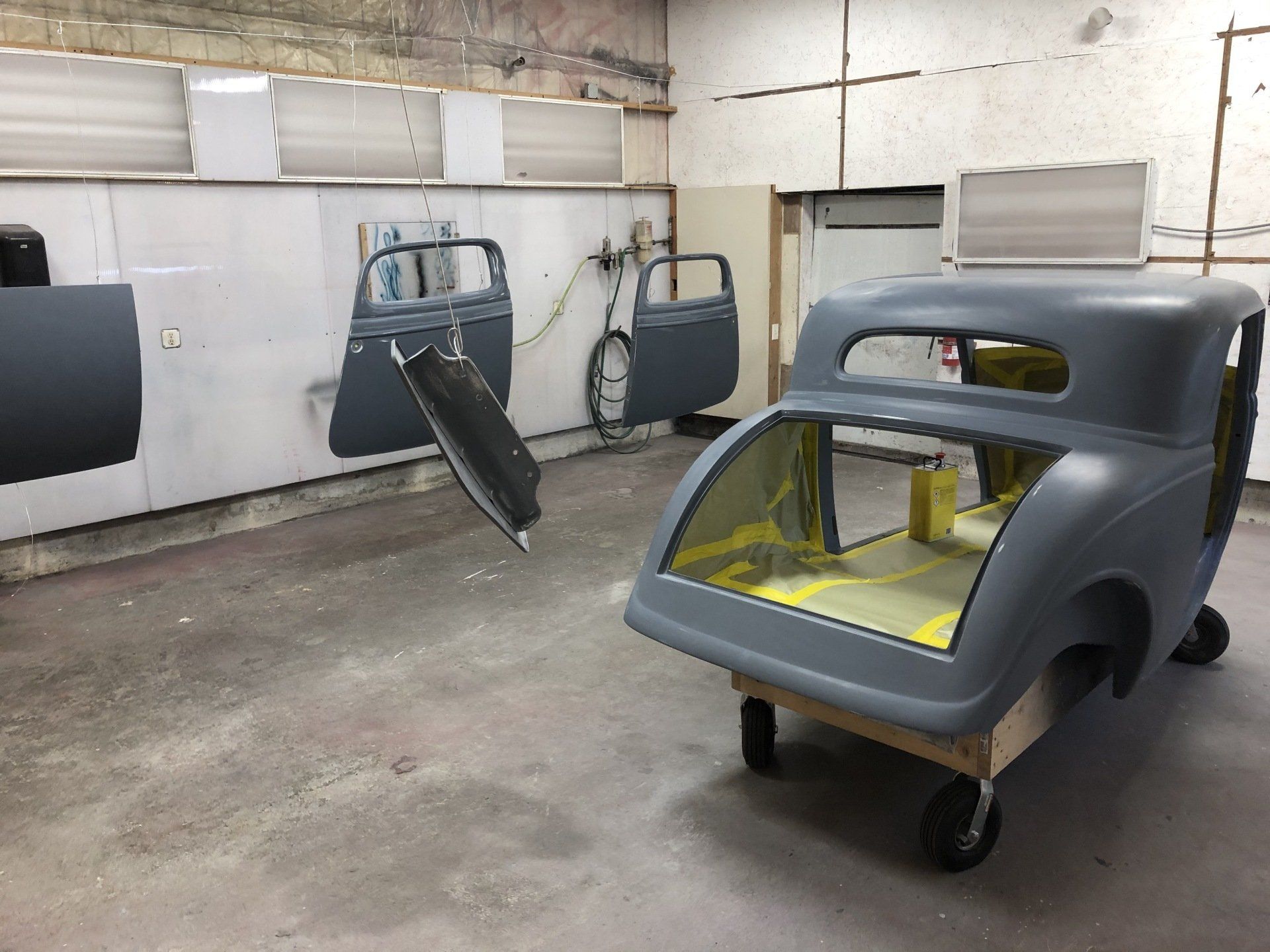 Workshop with a gray car body shell and detached doors on a concrete floor.