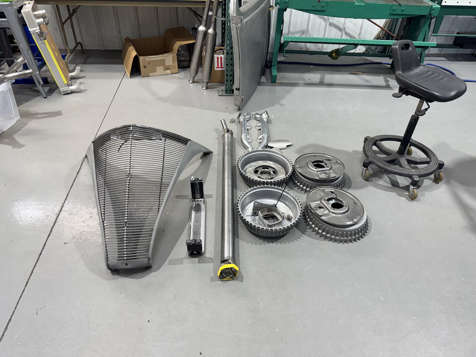 Workshop floor with assorted car parts, tools, and a rolling stool