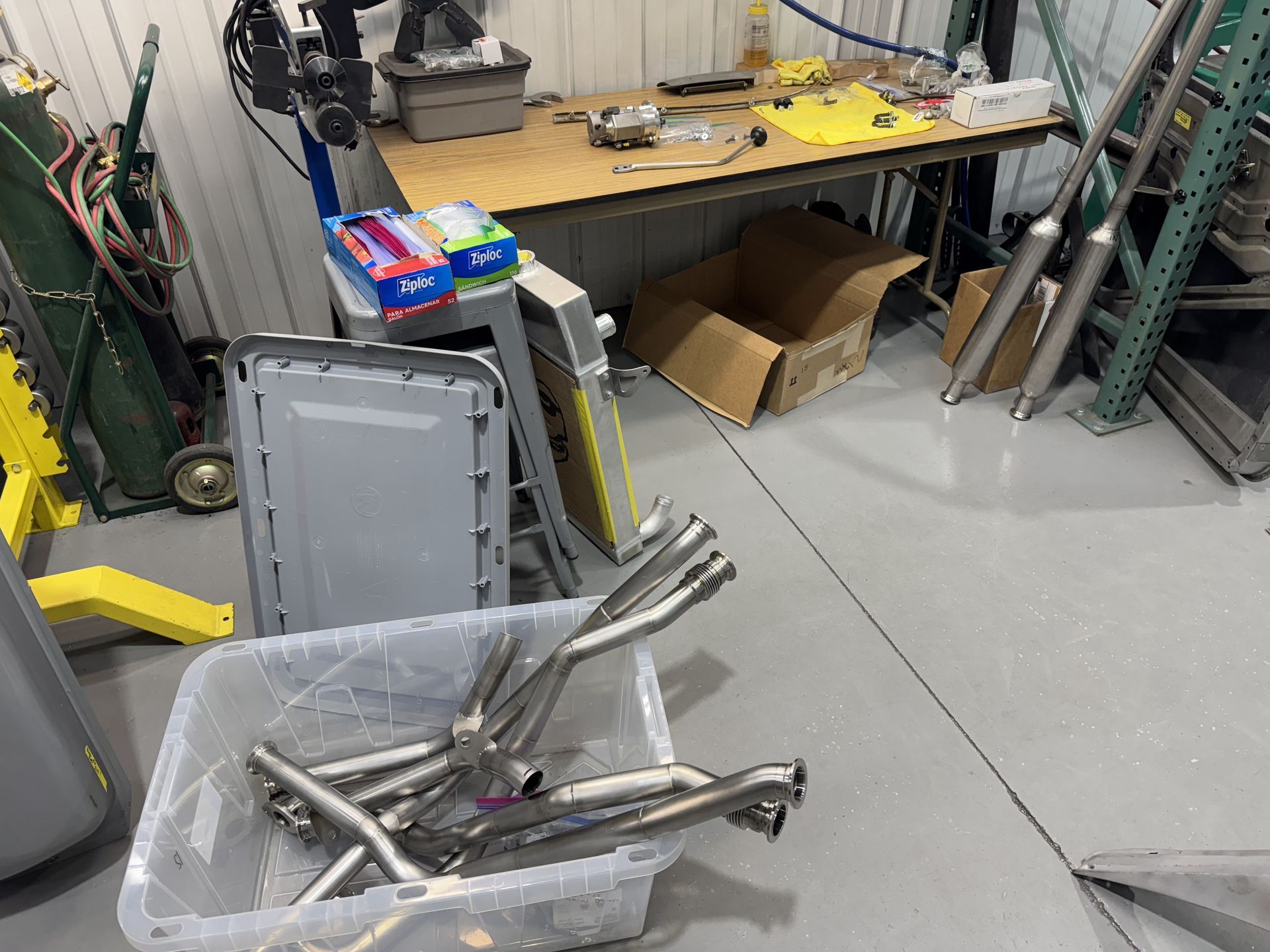 Workshop with a trash bin of metal parts, a workbench, cardboard boxes, and ladders against the wall