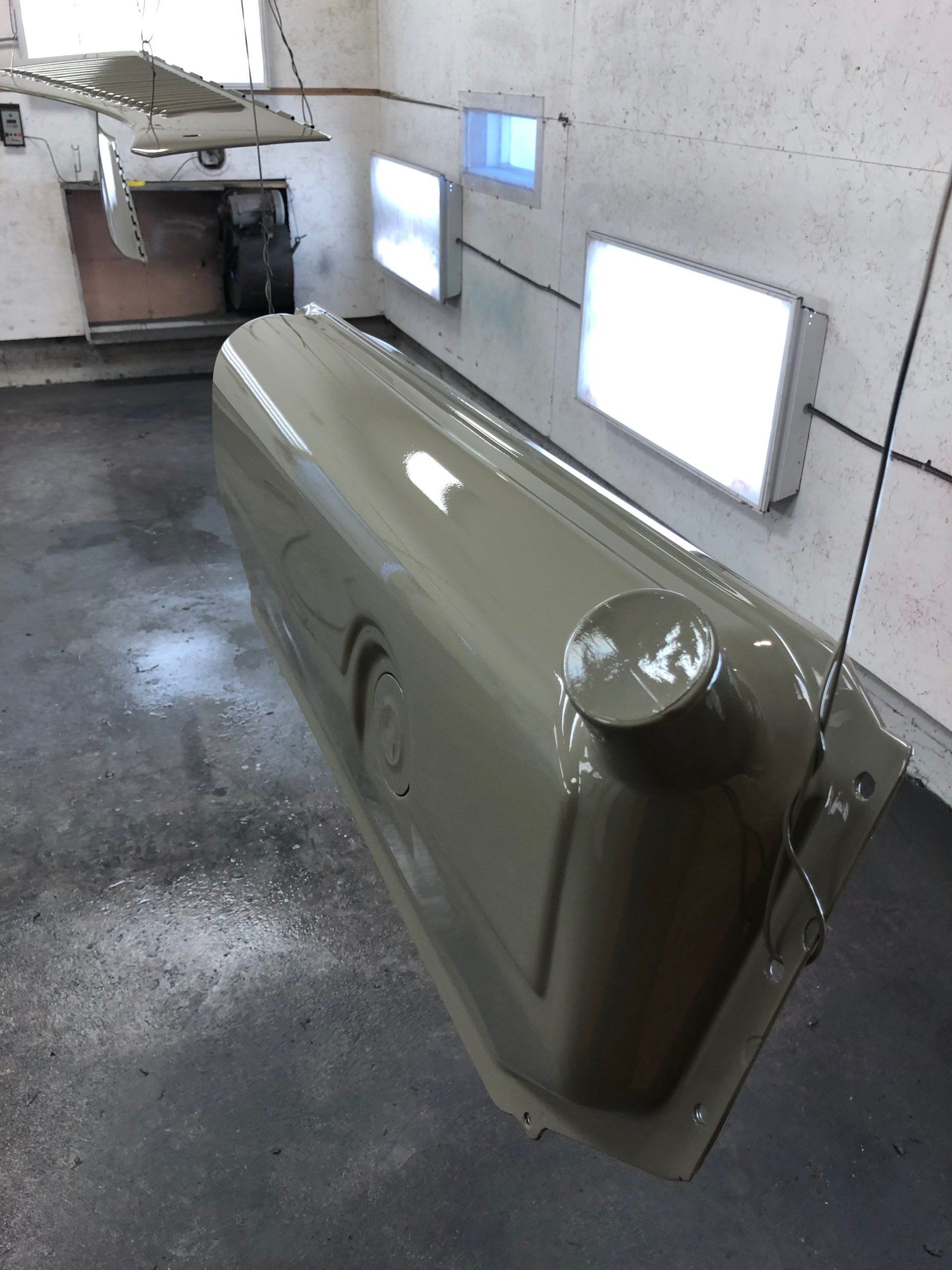 Olive green car door hanging in a spray booth with bright inspection windows