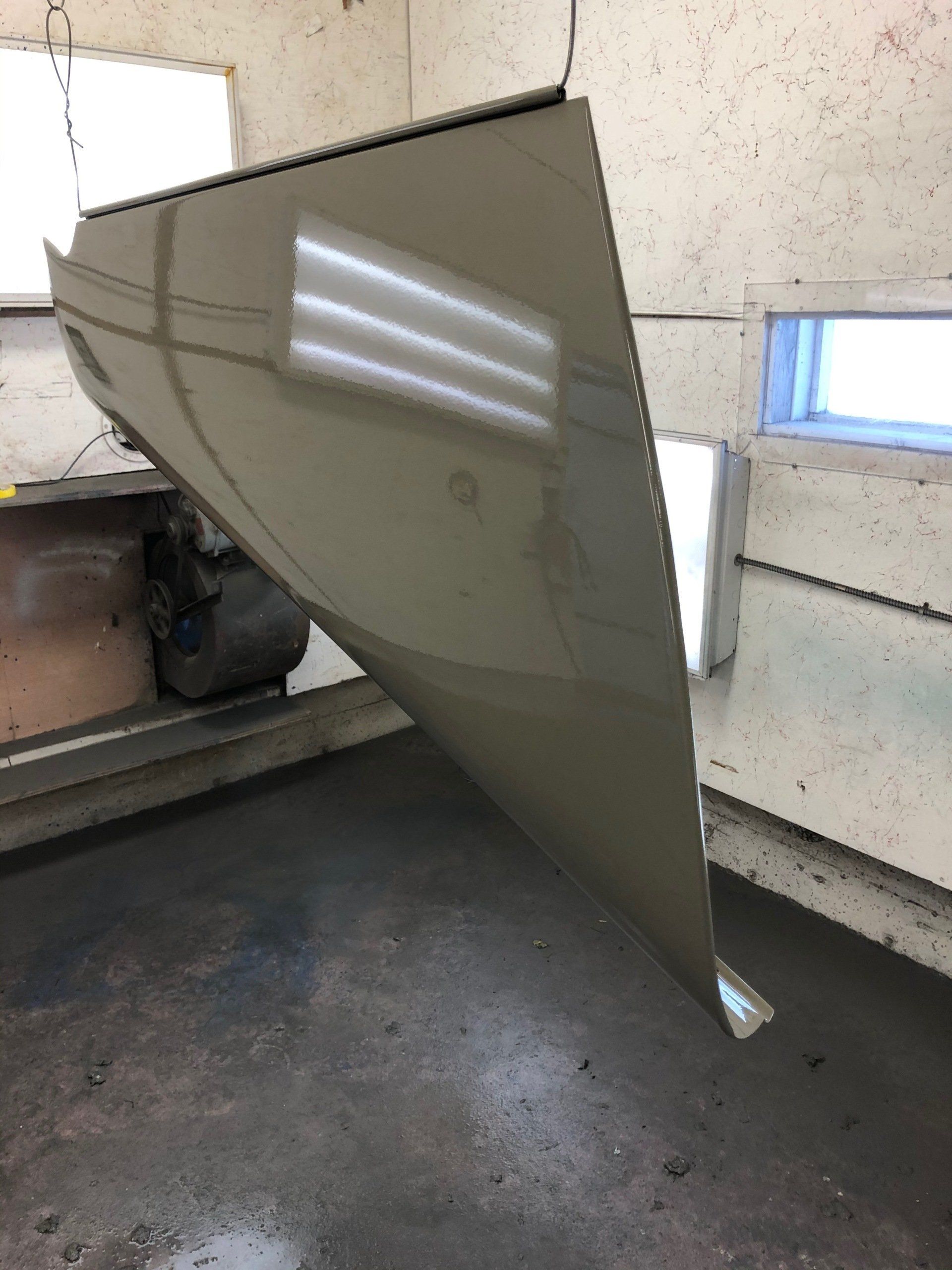 Large tan metal panel propped in a garage, leaning beside a vehicle.