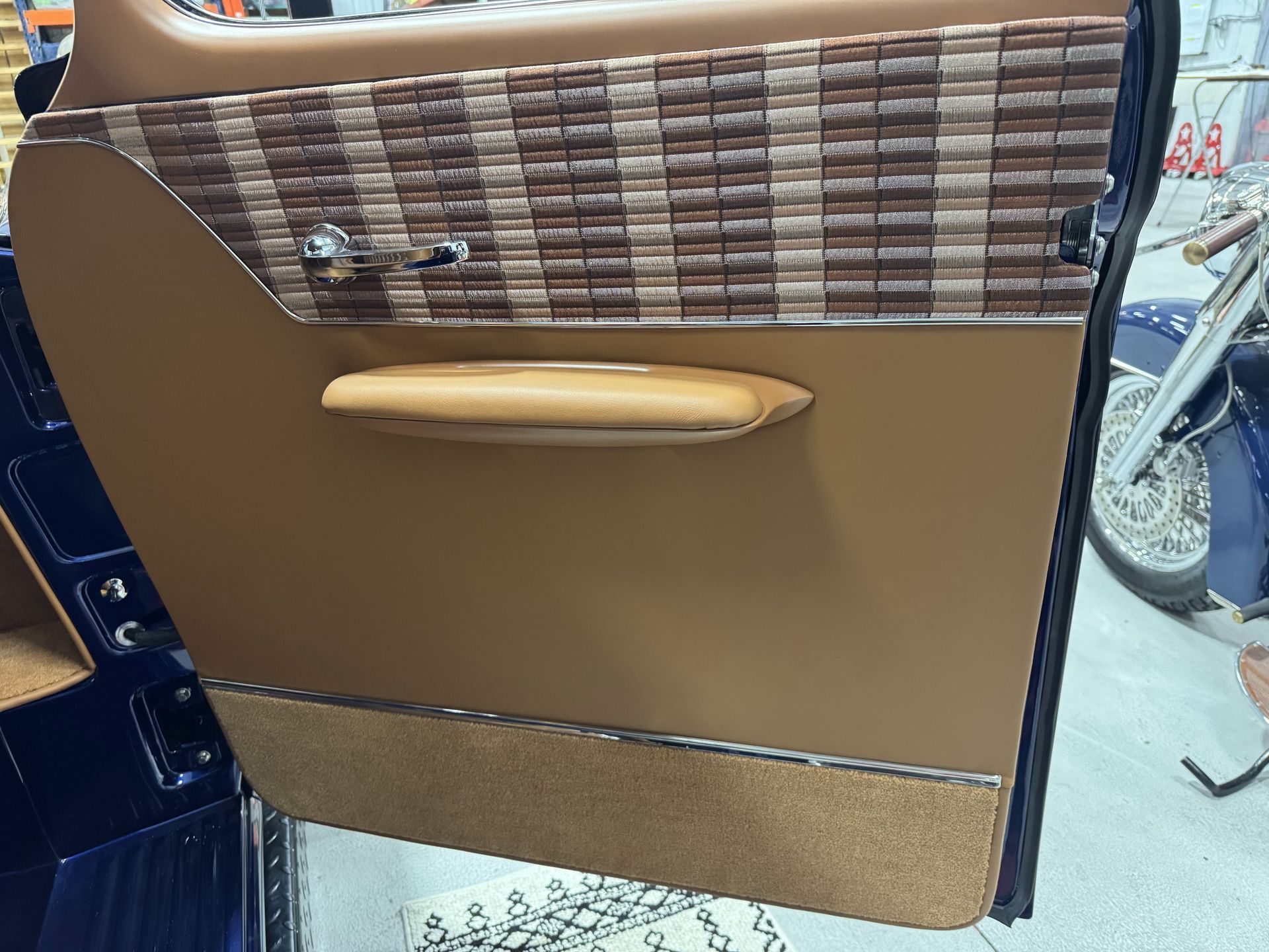 Car door interior with brown panel, woodgrain trim, and beige pull handle.