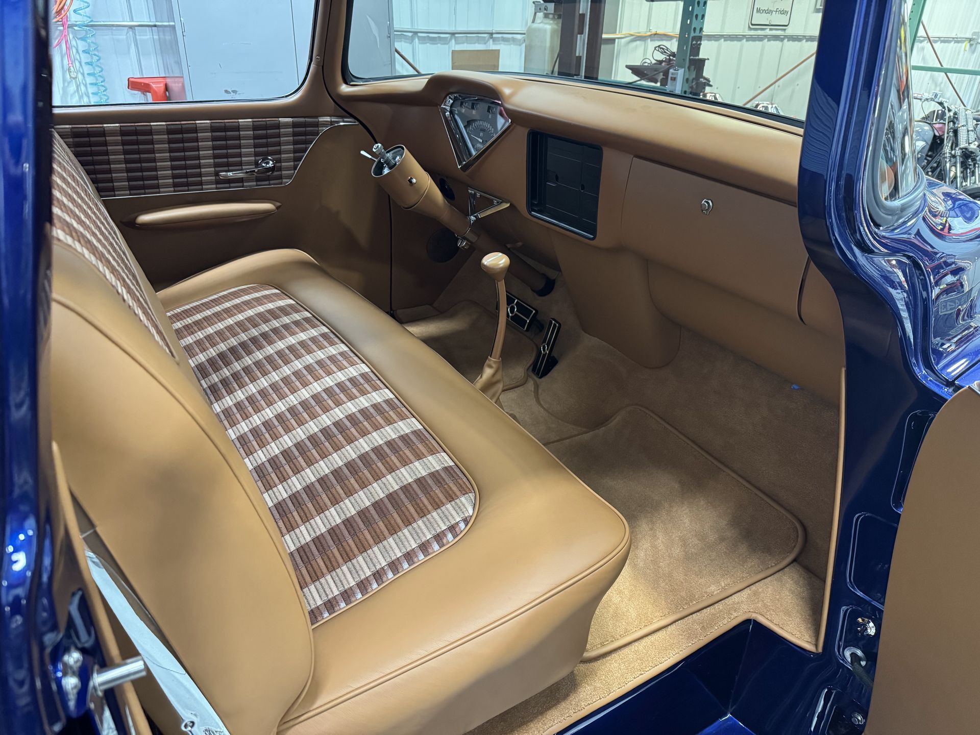 Classic car interior with tan upholstery, plaid bench seat, and steering wheel on the left.