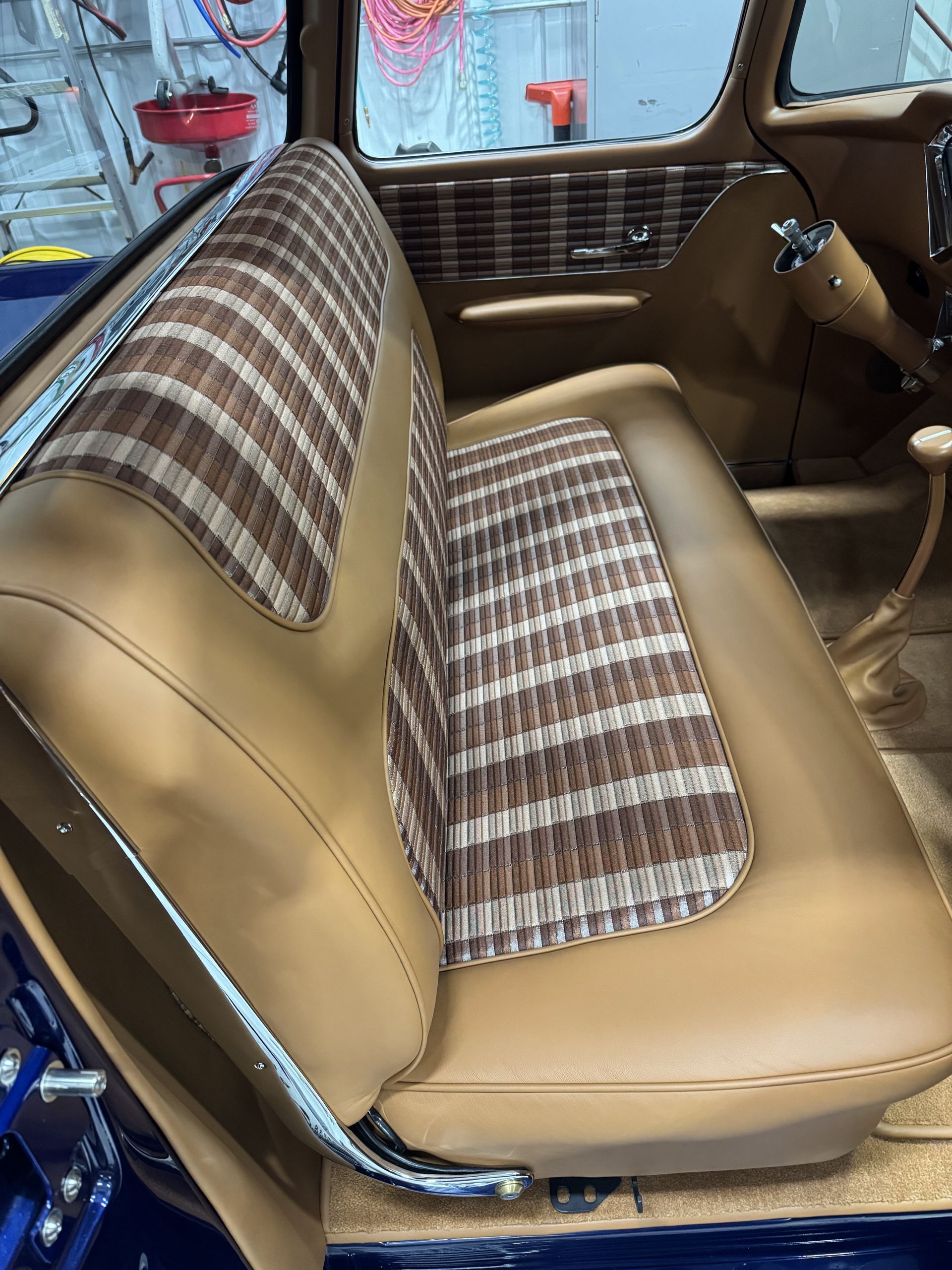 Tan plaid and tan vinyl car bench seat interior with blue exterior visible outside the door