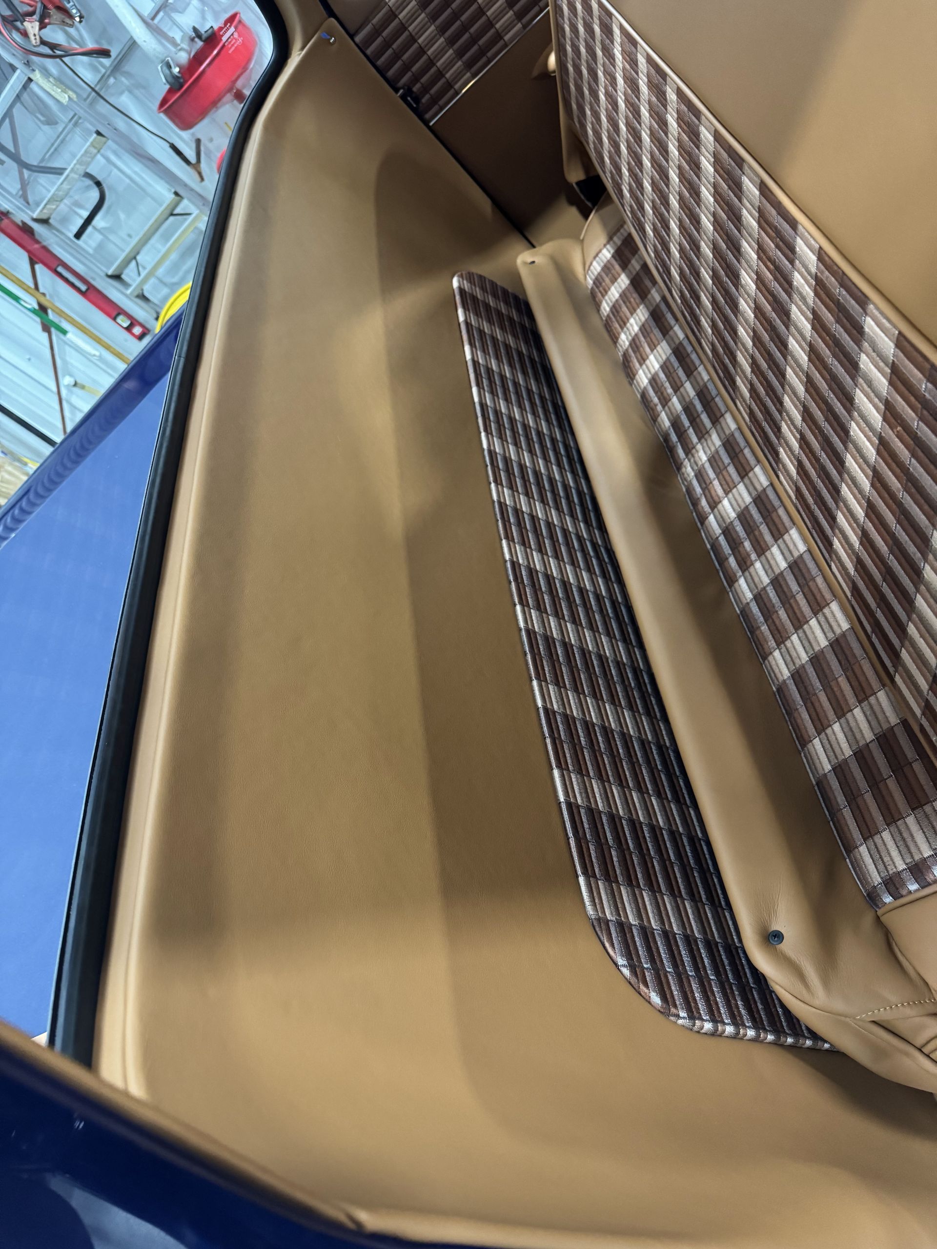 Open blue suitcase with beige lining and plaid straps on a tiled floor.