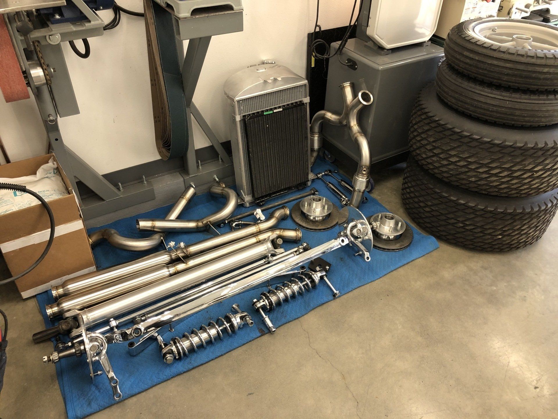 Auto parts laid out on a garage floor, including exhaust pipes, a radiator, and stacked tires.